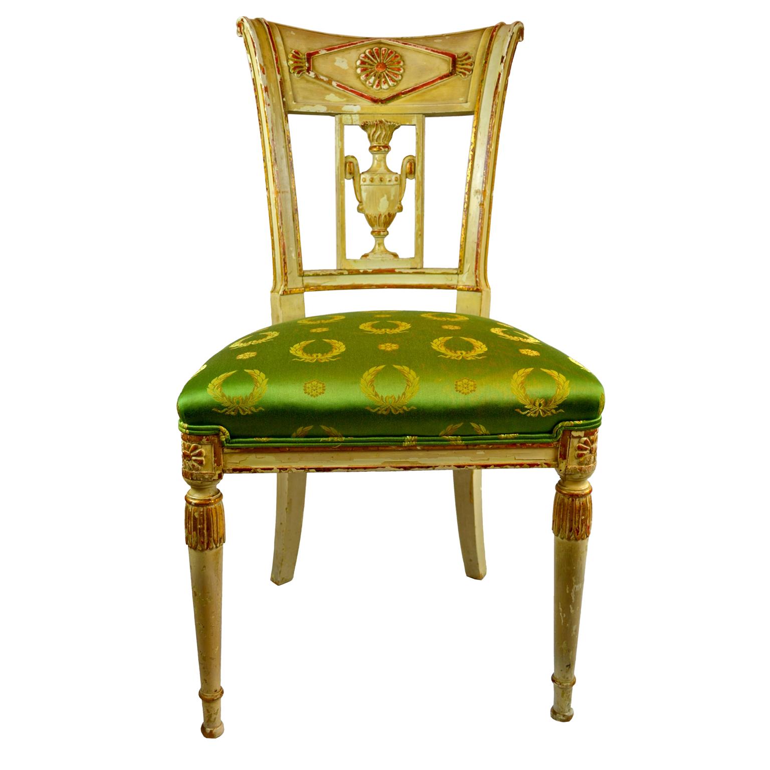A late 18th century French side chair from the Directoire Period with a carved and parcel gilt cream painted frame. The backsplat with a carved classical urn. Upholstered in green Empire silk fabric.