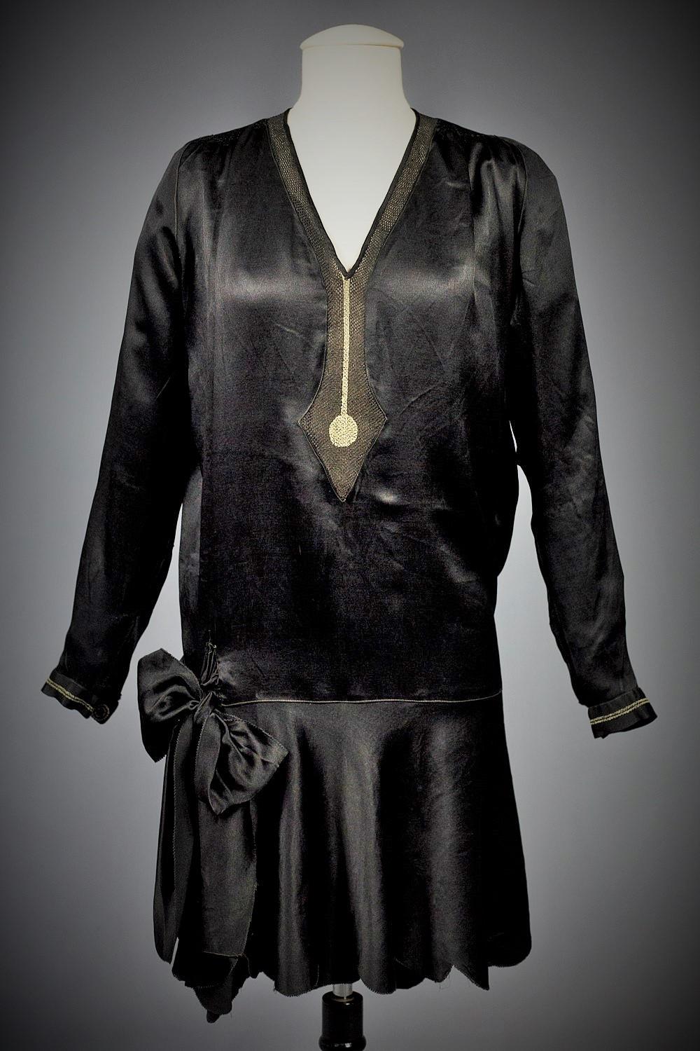 Circa 1920
France
Amazing little black dress, probably Haute Couture, with a minimalist graphic representing a drop of water and dating from the 1920s. Straight bag dress, V-neck, long sleeves in black Duchesse satin with a waxed sheen. Short skirt