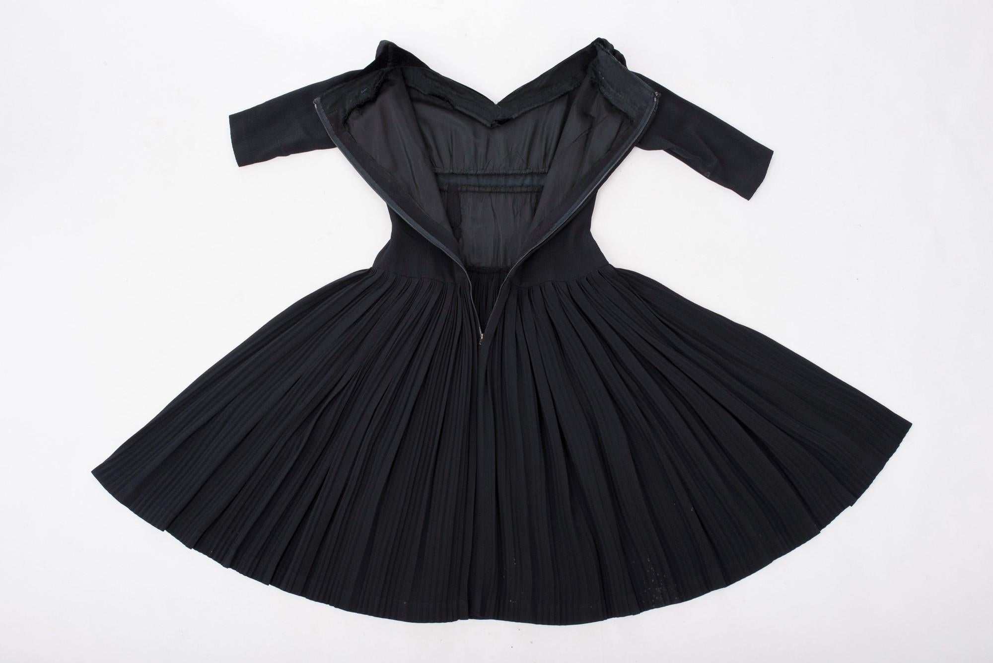 Circa 1955 France
Petite robe noire et son boléro par Nina Ricci et signés Paris 55. Pouf en soie stretch noire avec des côtes parallèles permettant un ajustement serré et surtout un travail intéressant de plis creux pour la jupe. Robe cintrée à