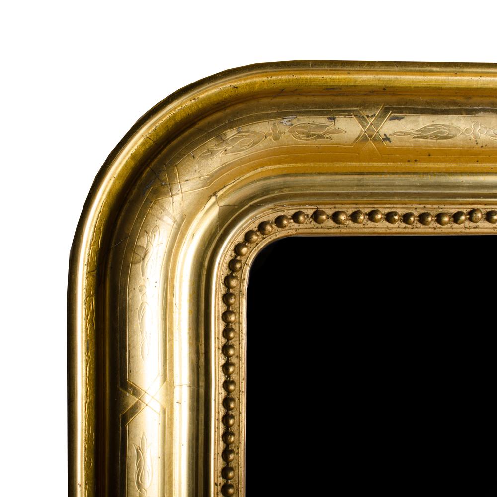 A large scale French Louis Philippe mirror circa 1830. The mirror features a delicately incised floral pattern and retains the original mercury glass mirror which is surrounded by a small interior beaded border.
