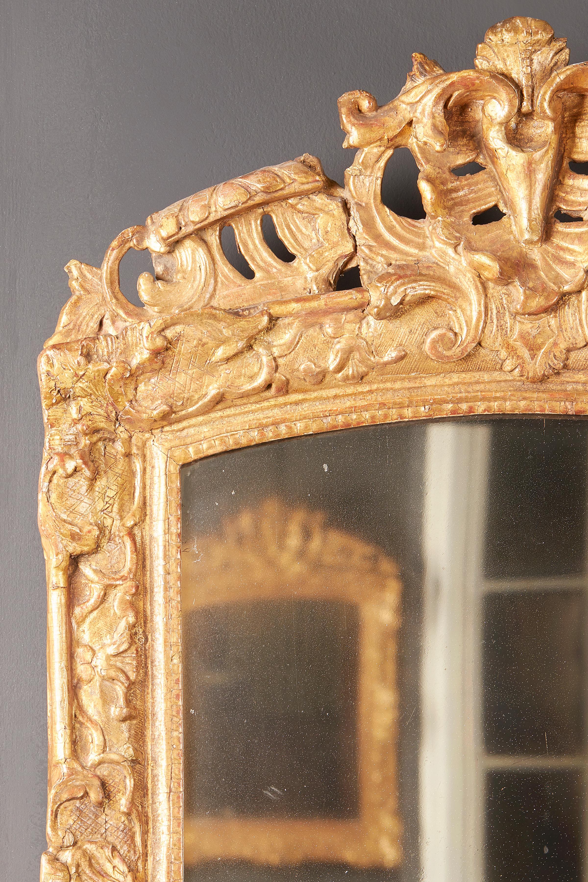 A French Louis XIV style carved gilt and gesso wall mirror, early 19th century, circa 1810-1830, with elaborate pierced shell and scroll pediment.