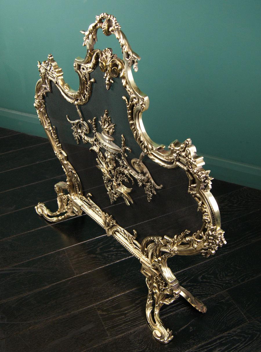 A French Louis XV brass fire screen in the Rococo form. 
The finely shaped frame with foliage, scrolls and grape detailing supported on four leaf-form feet.  Central urn with flame and floral work above two birds set on black mesh. An intricate