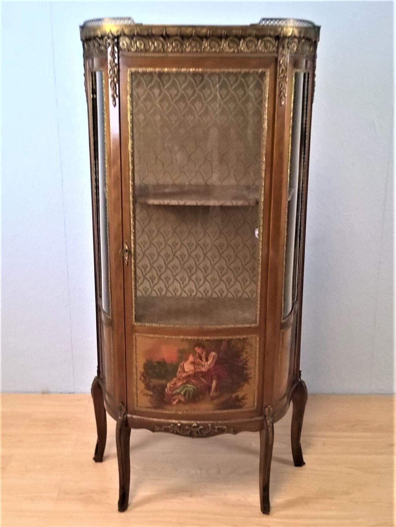 A French Louis XV Revival mahogany vitrine with metal mounts and hand painted scenes
The marble top with a brass gallery decorated with swags and scrolls.
The bow fronted glass door encloses a lined interior with two shelves and a serpentine