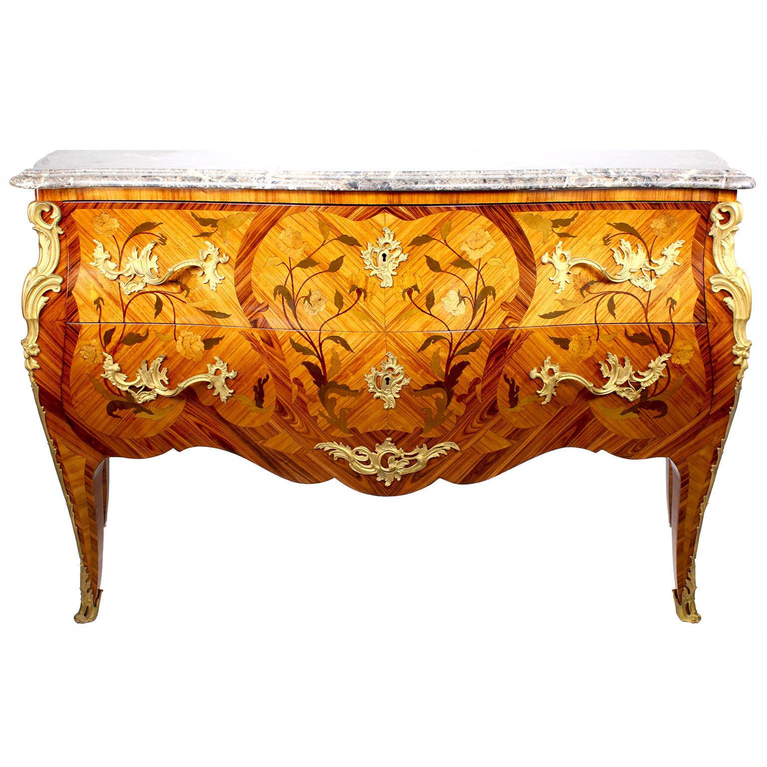 A French Louis XV Style bois satiné, kingwood and amaranth - Ormolu Mounted Two-Drawer Bombé Commode with mottled marble top. The bowed front and sides with floral marquetry and floral ormolu handles with decorative elements. The top carcass