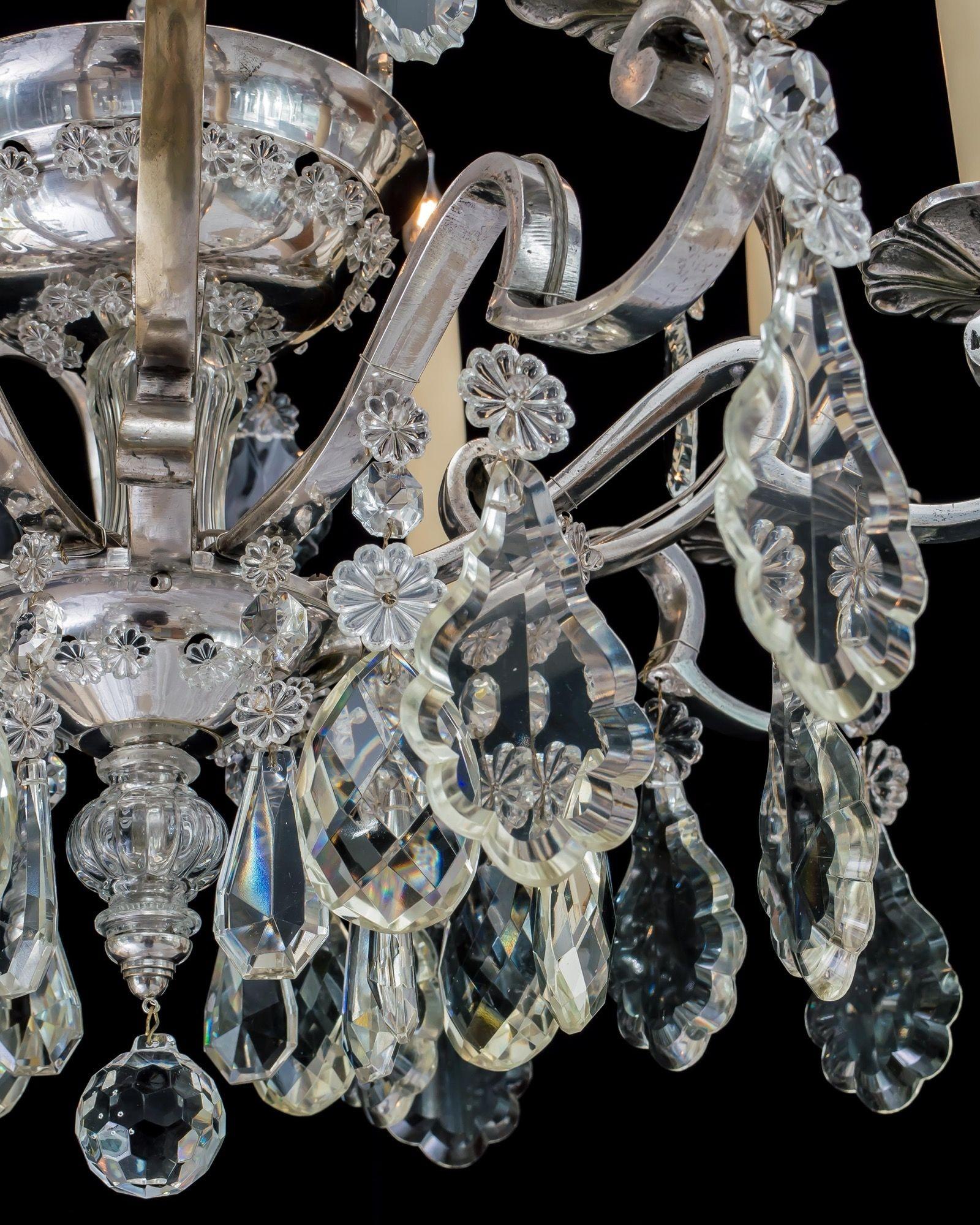 A silvered cage chandelier with eight candle arms, all hung with cut glass flakes. A central silver bowl decorated with glass rosettes and internally illuminated.