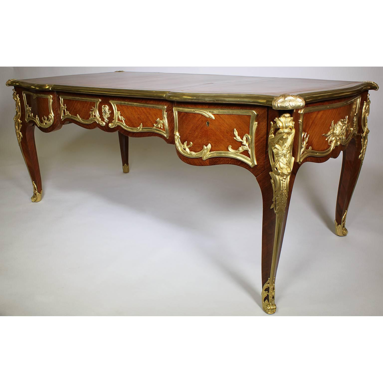 A French Louis XV style gilt bronze-mounted kingwood bureau plat (desk). The gilt banded rectangular top set with gilt bronze acanthus mounts at the corners centering a gilt banded inset leather writing surface with three apron drawers and raised on