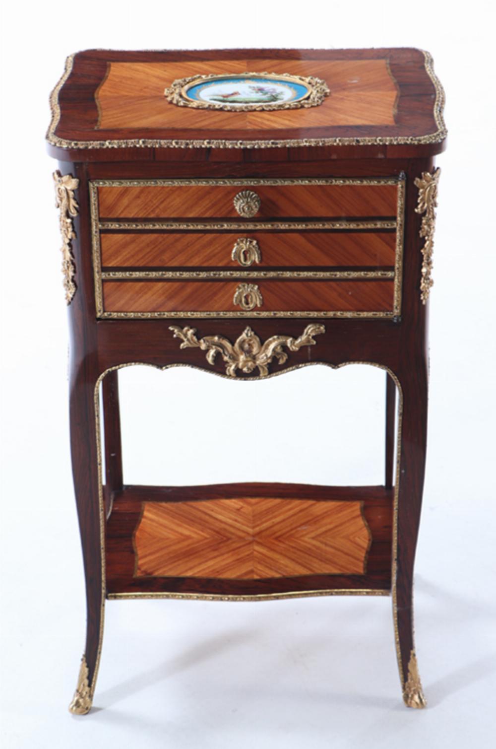 Questo grazioso mobile ha un piano con una placca in porcellana stile Sèvres dipinta con uccelli, sopra una cassa con un'anta singola montata in bronzo con una finta facciata a tre cassetti. La cassa e il ripiano inferiore sono uniti e sostenuti da