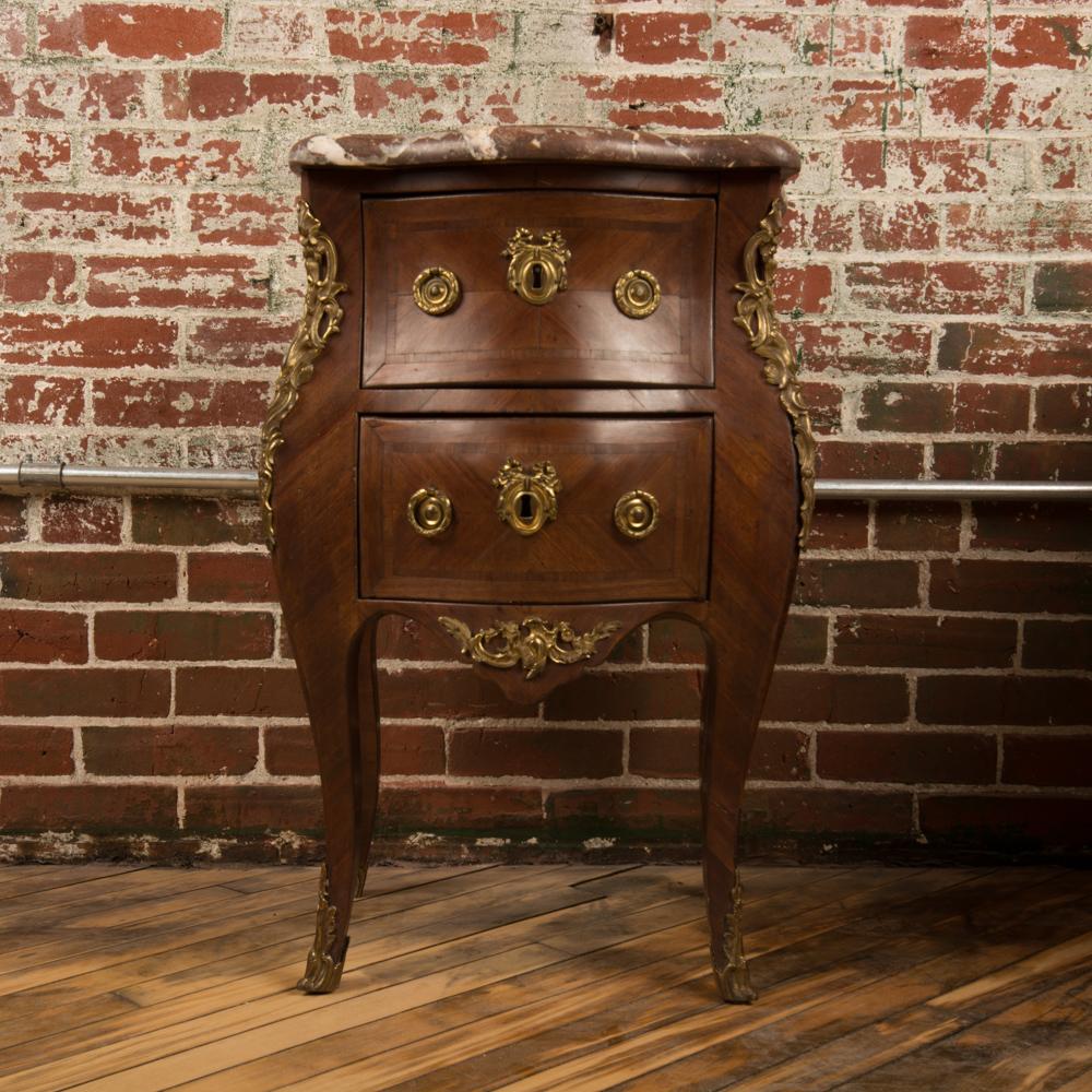 A French Louis XV style marquetry side cabinet, circa 1940. The nightstand features mahogany wood grain and a red beveled marble top. The nightstand offers two drawers, and the case rests on cabriole legs with mounted ormolu details.