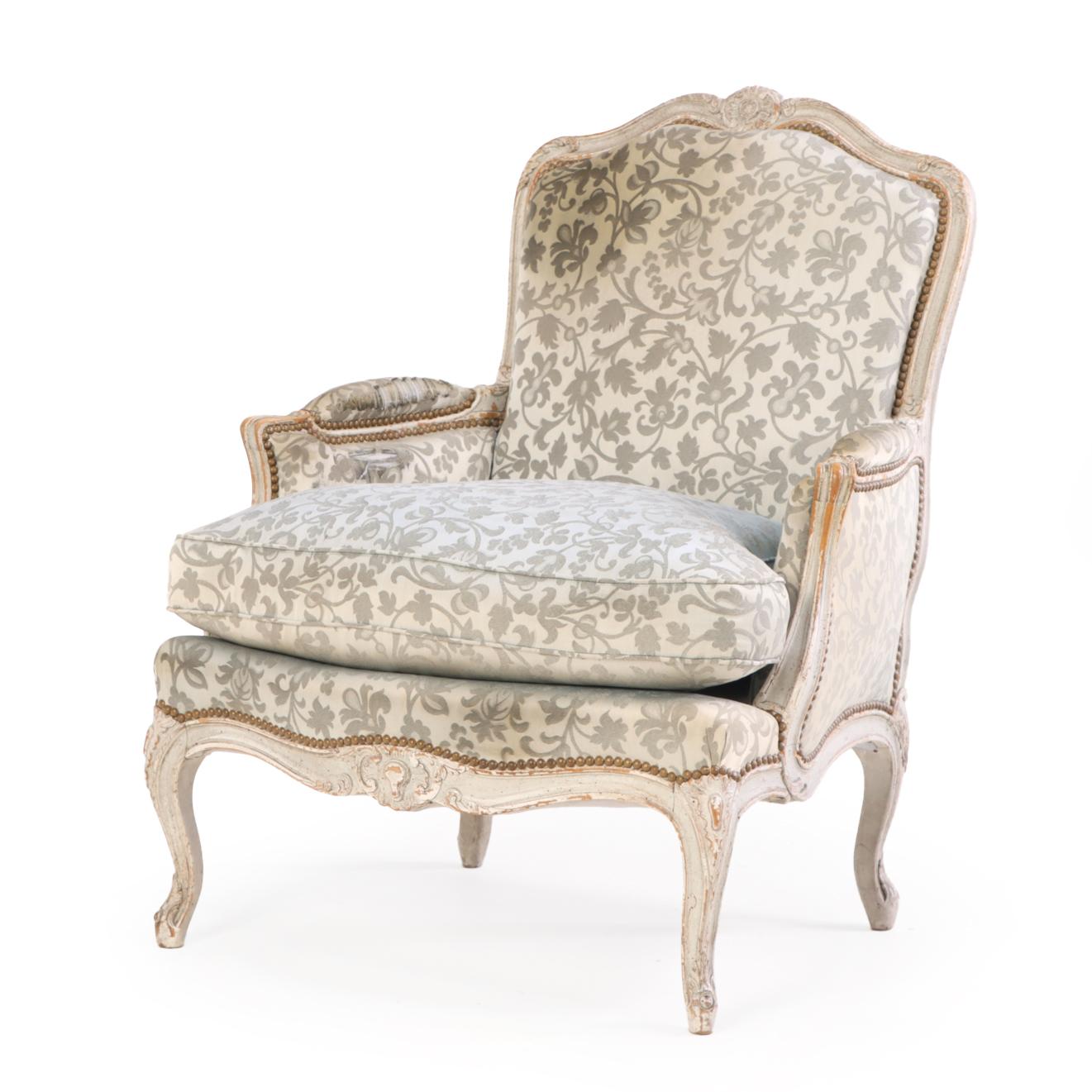 Bellamente detallada, esta bergère clásica presenta un armazón tallado y pintado con brazos en volutas y patas cabriolé, tapizado en una tela azul Fortuny. La combinación de pintura texturizada y lujoso textil resalta la intemporal mezcla de