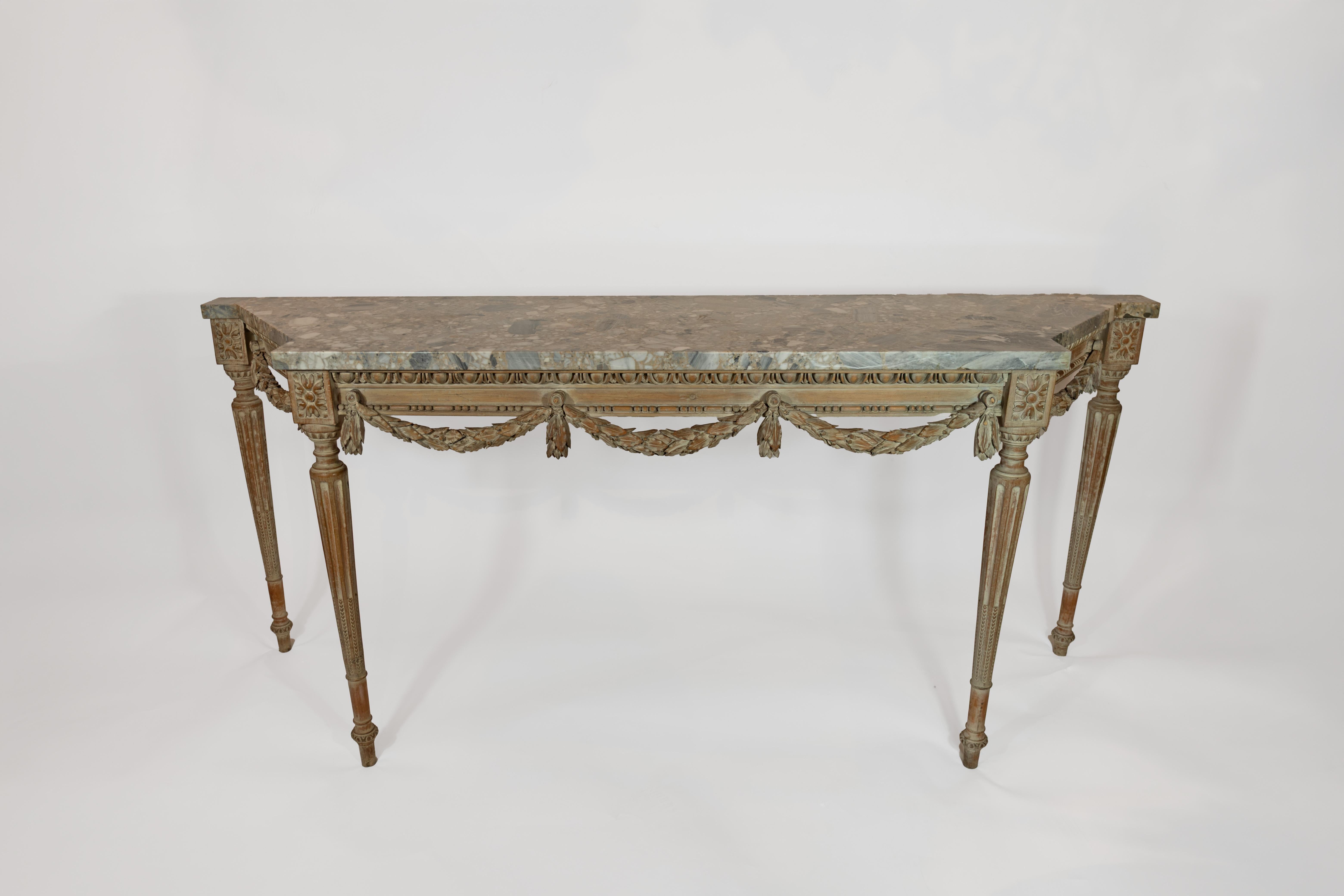A French Louis XVI-style console with carved apron having egg and dart molding draped with bellflower garland. The four round and tapered legs with stop fluting below rectangular corners with carved rosettes. The apron supporting a stone top with