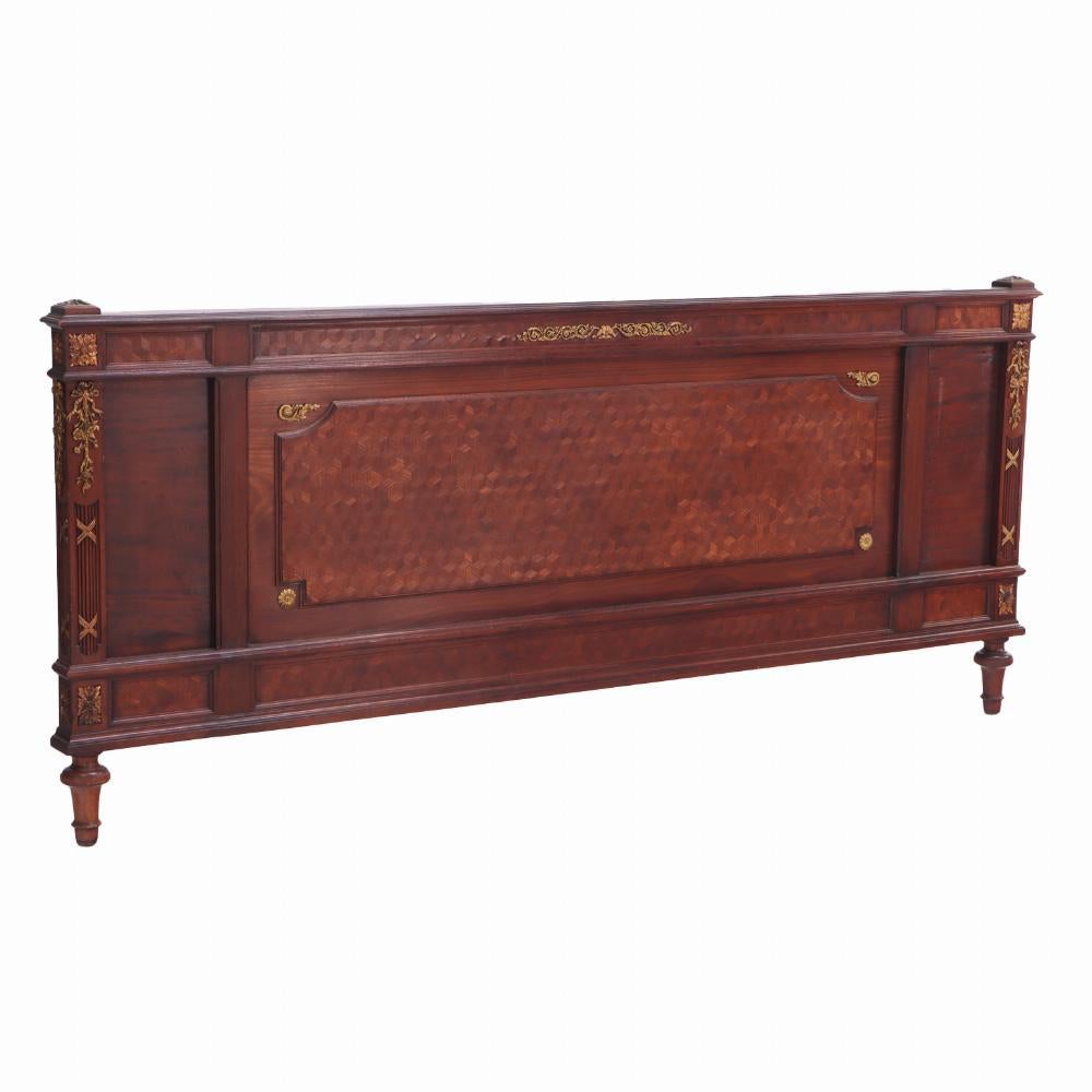 This stately bed has parquetry inlay adorned with gilt bronze mounts, the headboard with a ribbon topped cartouche flanked by floral guilloche and finials, the conforming footboard mounted similar embellishments, all raised on shaped