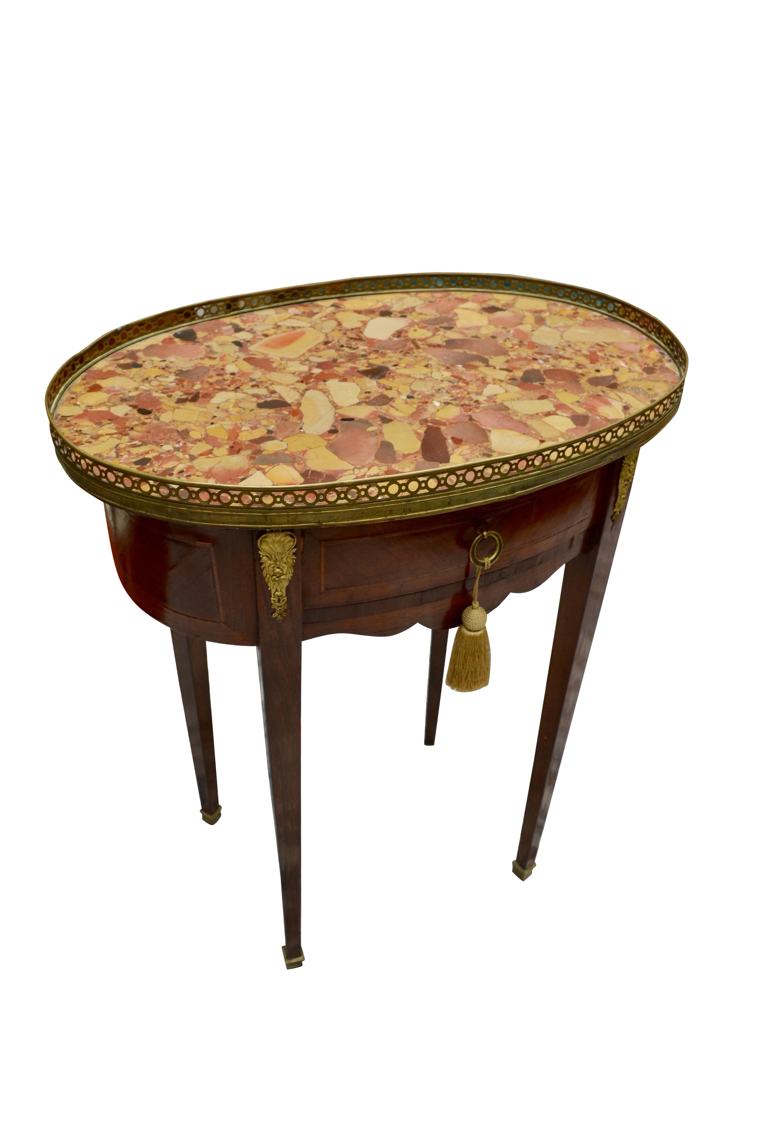 The frame of this oval table is veneered in various exotic woods, kingwood, amaranth, tulipwood. There is one drawer below a galleried brocaatel marble top. The table sits on four tapered straight legs with gilded metal mounts at the top and brass