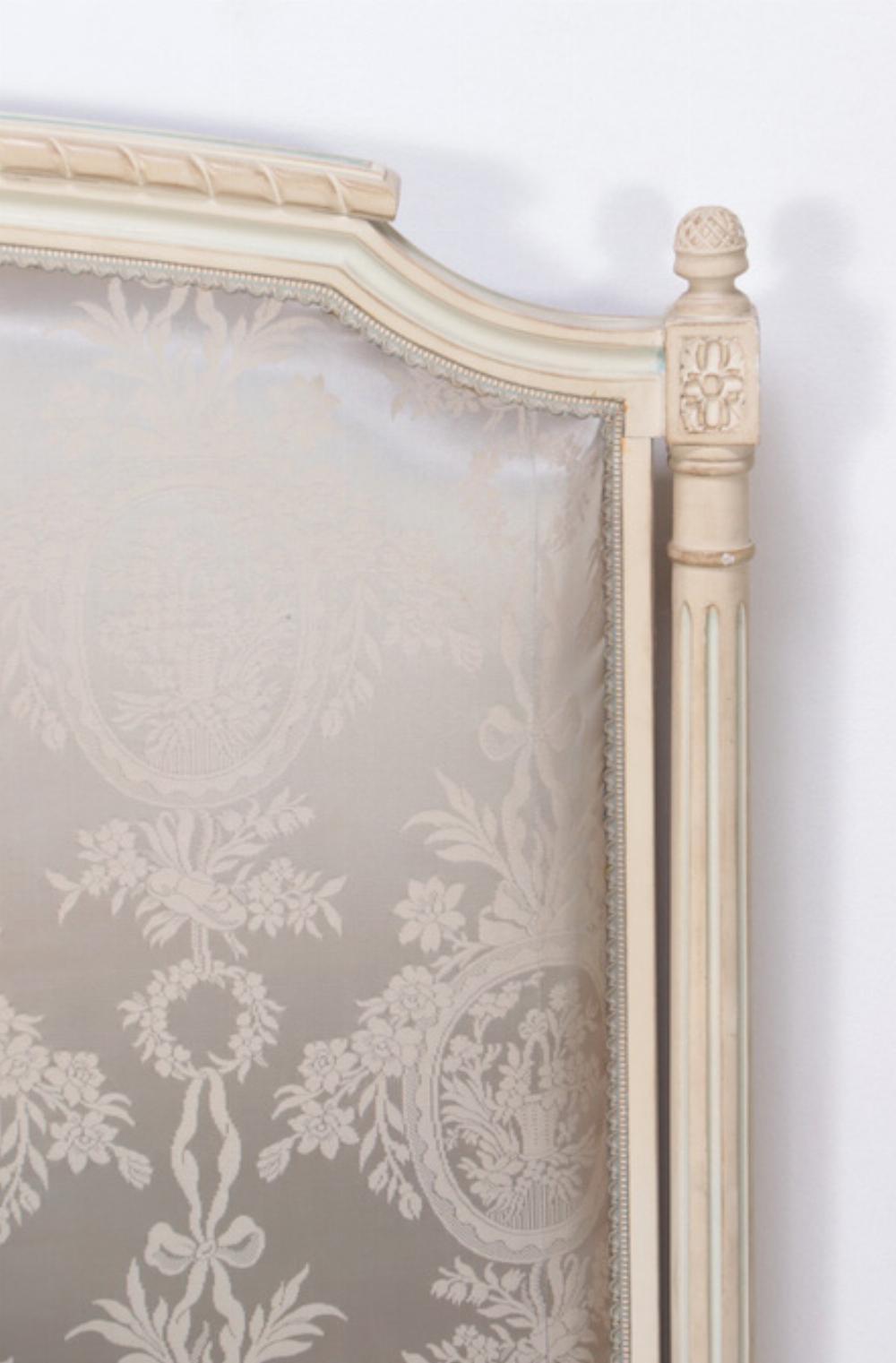 A French Louis XVI style painted and upholstered full size bed C 1940. The carved and shaped frame having turned finials and silk upholstery.