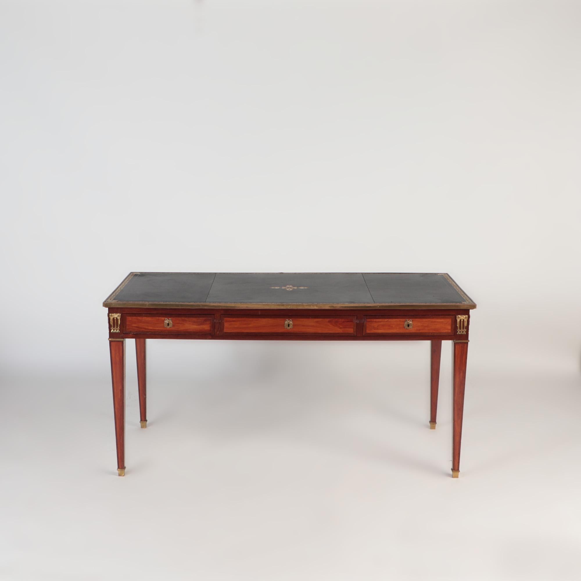 A French Louis XVI style three drawers writing desk or bureau plat. The desk has a leather top writing surface, three locking drawers with false drawer fronts on the opposite side of the table. Square tapering legs ending in brass sabots.19th C
