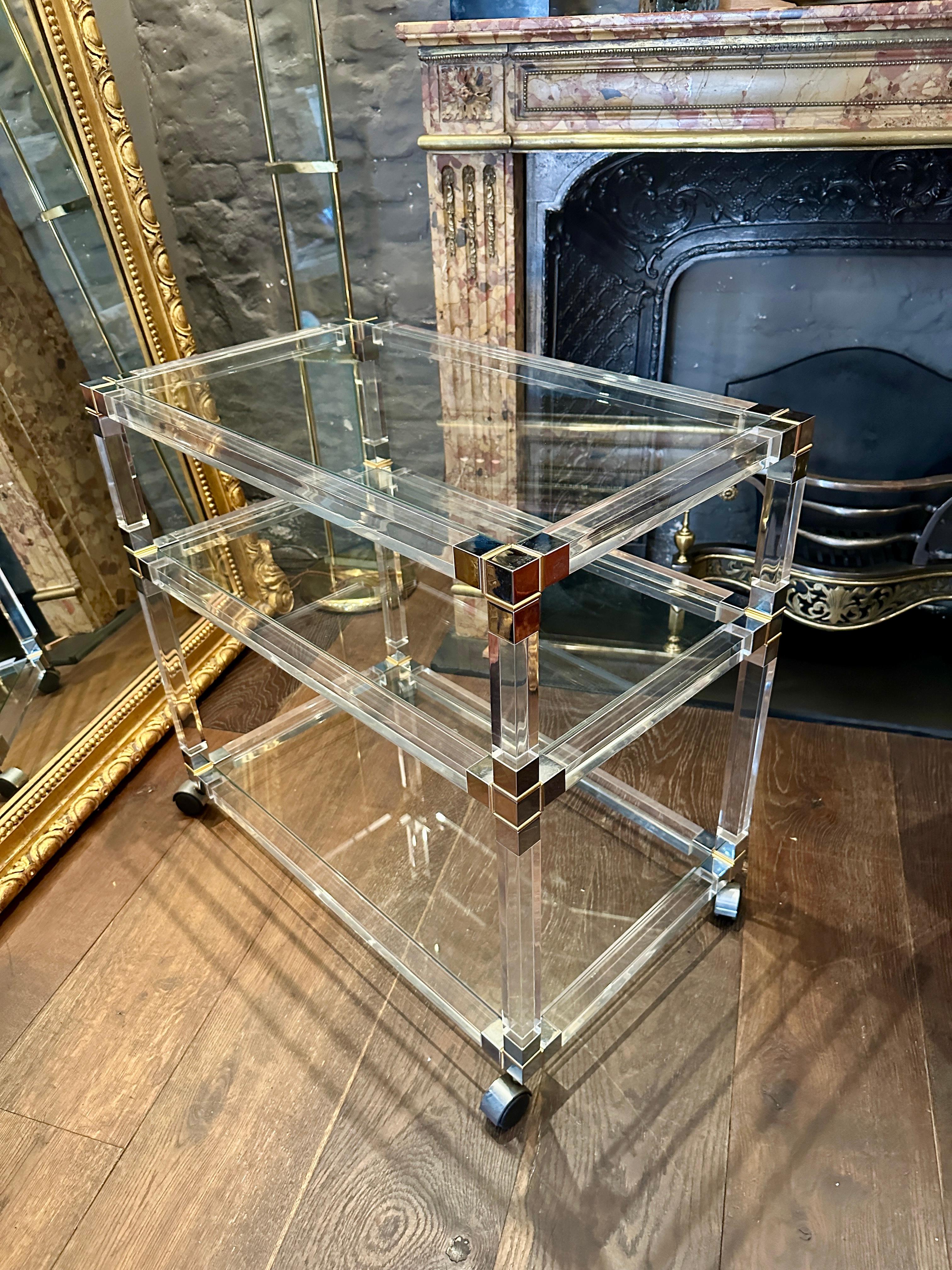 A large French bar cart in lucite brass and chrome, with 3 staggered tiers, chrome covered black castors. The chrome corner pieces with brass accents, supporting clear and in good condition lucite frame. 

French late 20th century 