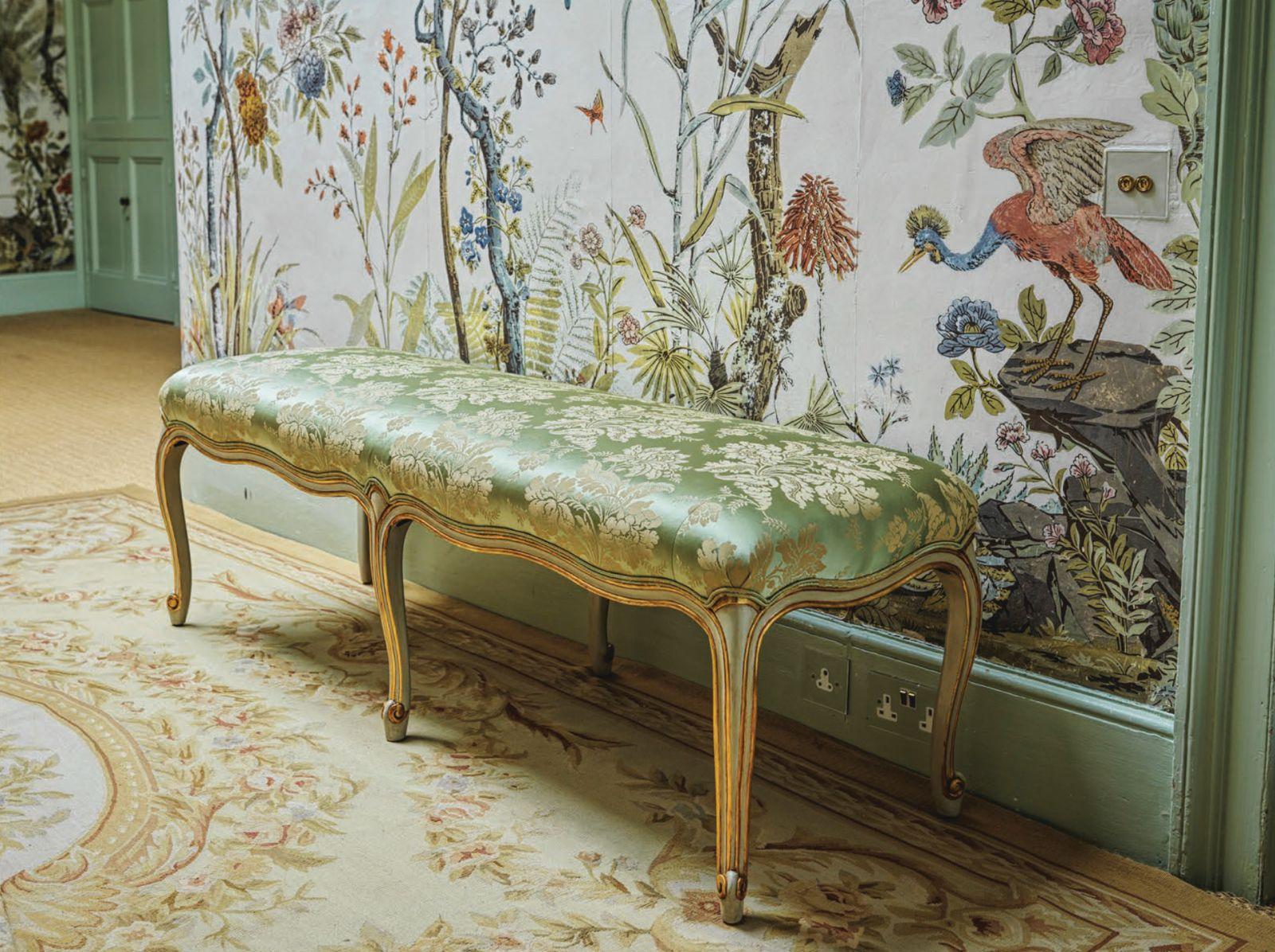 A French Louis XV Style Bench, all hand carved, featuring curved line work and serpentine legs. The piece's carving is further enhanced with a two tone, hand-finished patina in celadon green paintwork with gilded highlights. The fabric is a silk