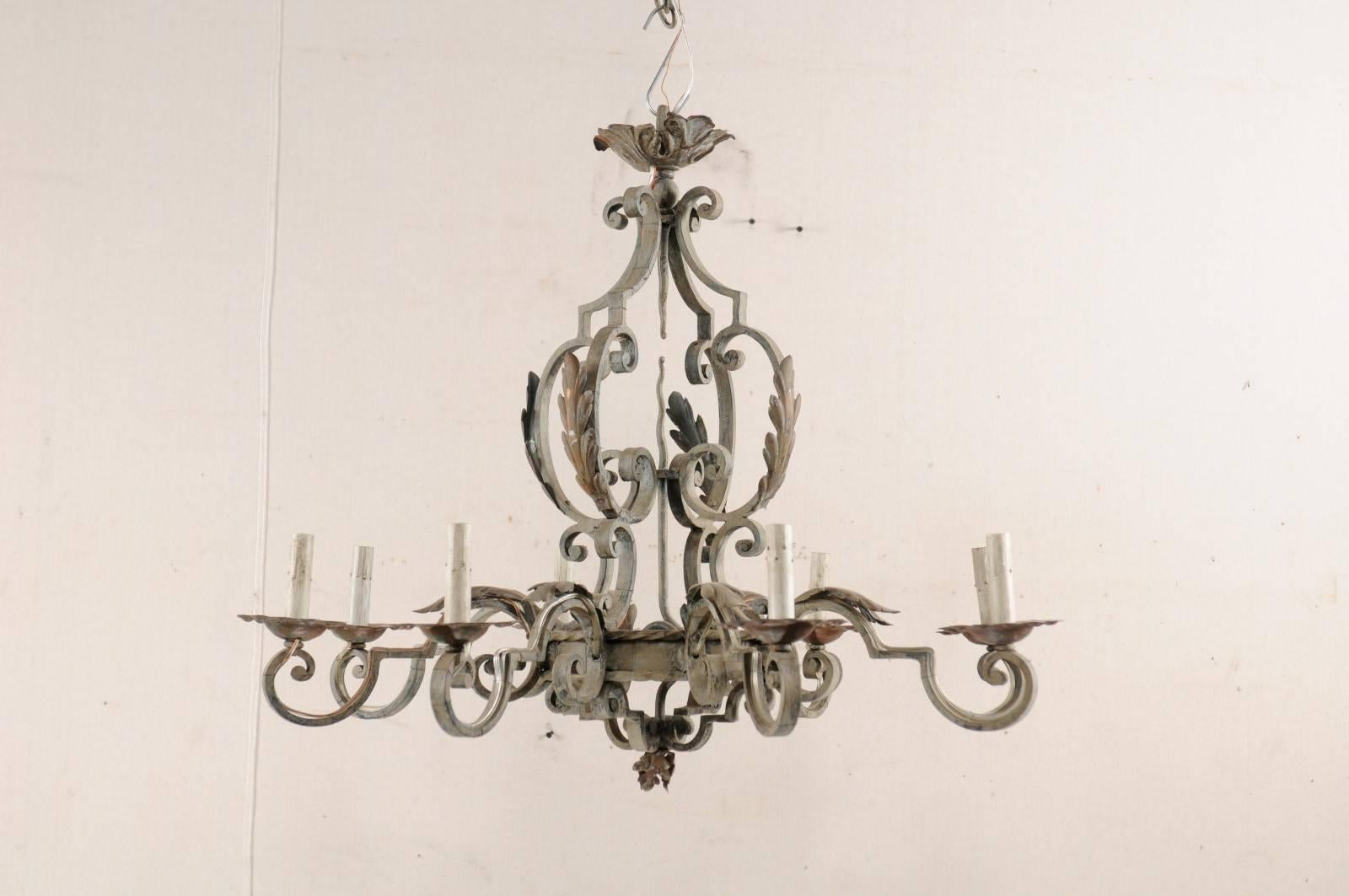 A French painted iron eight-light chandelier from the mid-20th century. This vintage French iron chandelier features a smaller centre ring with roped accent detail at its upper edge, surround by a decorative armature of scroll work, and adorned with
