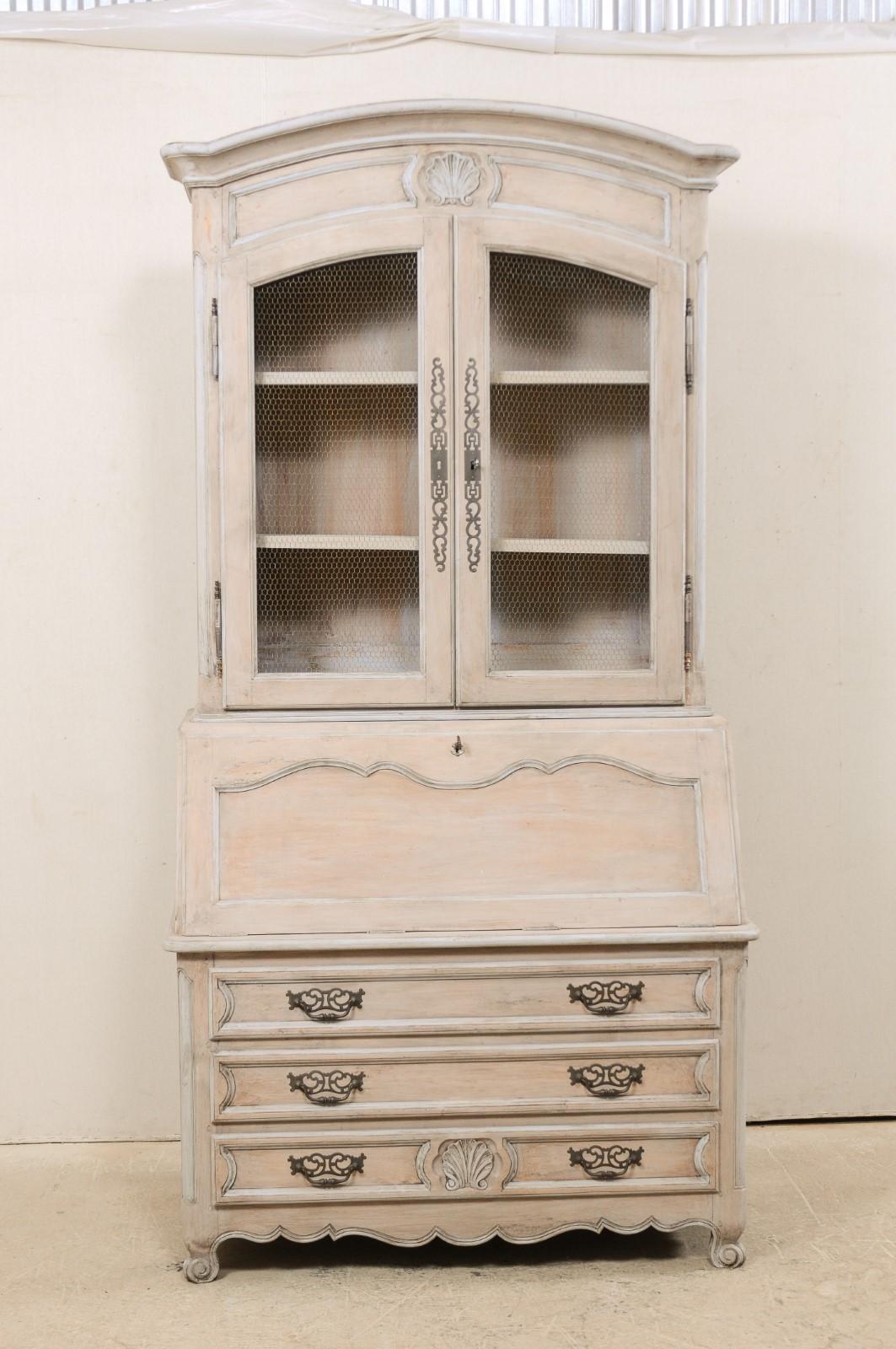 A French display curio cabinet with slat front desk from the mid-20th century. This vintage cabinet from France features an upper curio cabinet with wire front doors, atop a slat-front writing desk, and chest of three graduated drawers beneath. The