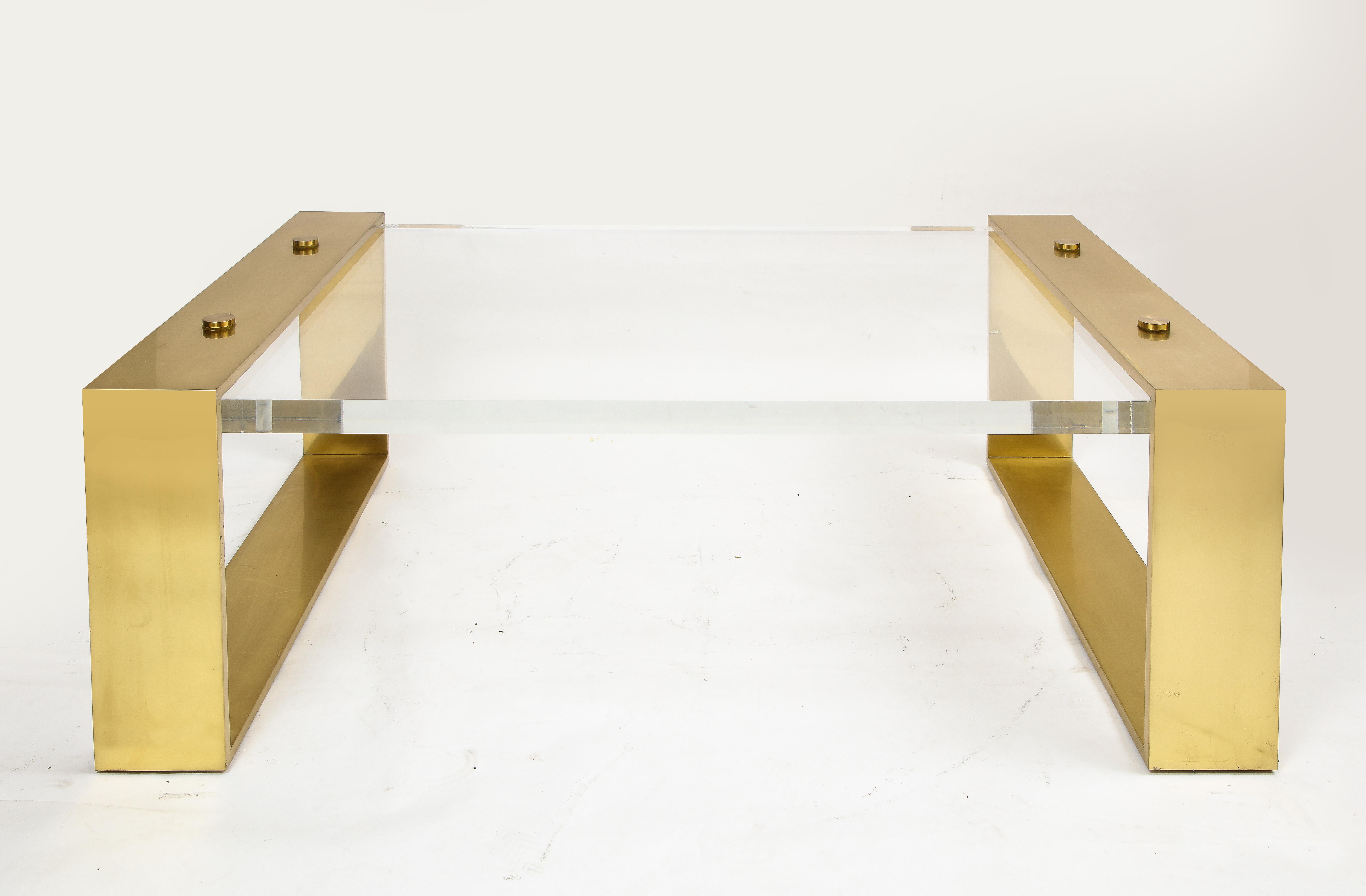 A Beautiful French Mid-Century Modern rectangular form gilt bronze mounted lucite center/coffee table. The legs are beautiful with two riveted bolts found on either side. Sandwiched between the legs is a thick clear lucite table-top which is held