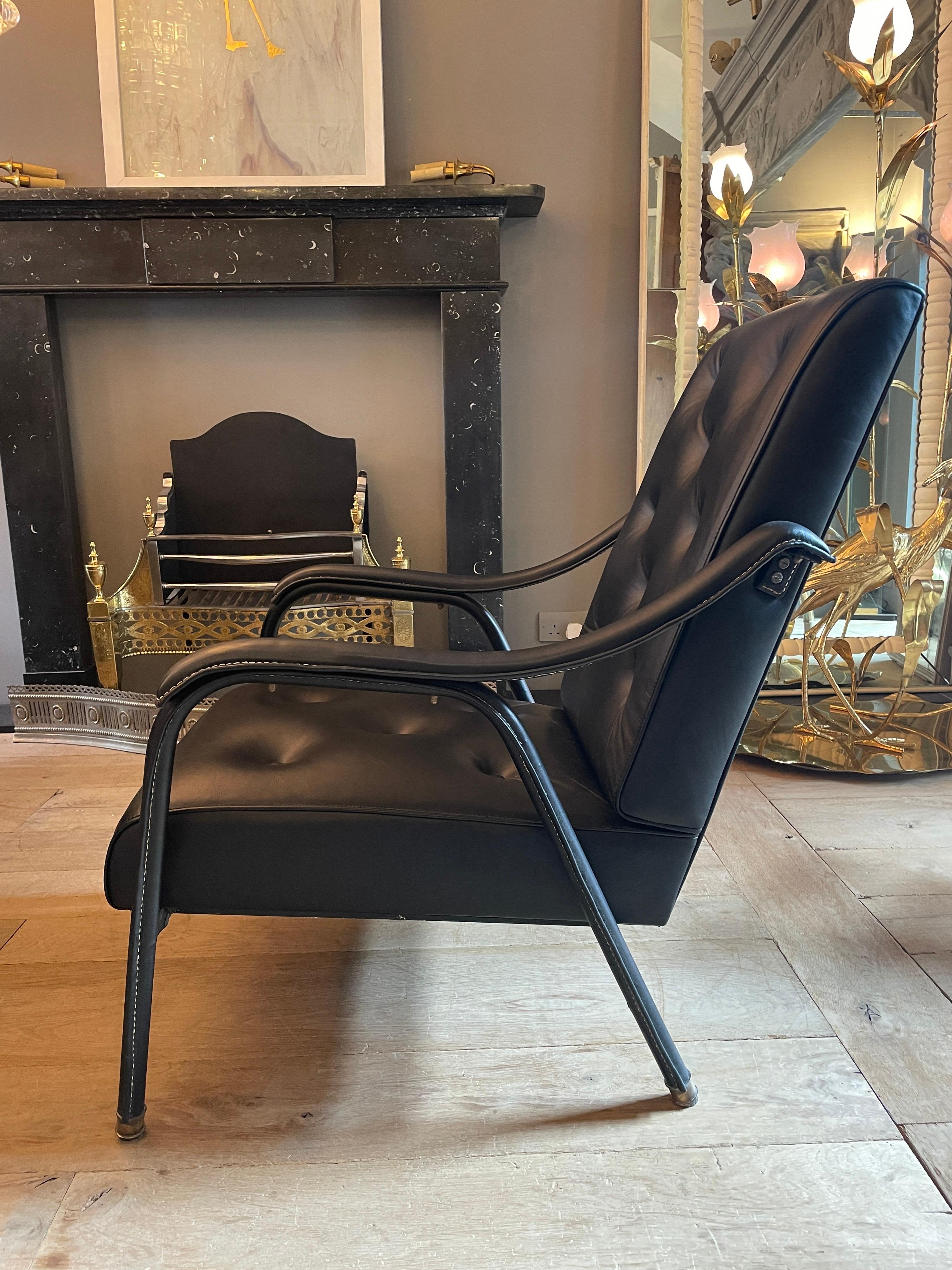 A black leather saddle stitched armchair, with buttoned back and seat. Brass accents and feet. By Jacques Quinet. In very good condition, previously restored. Images a true reflection of the condition of this piece. 

For reference Guitemie