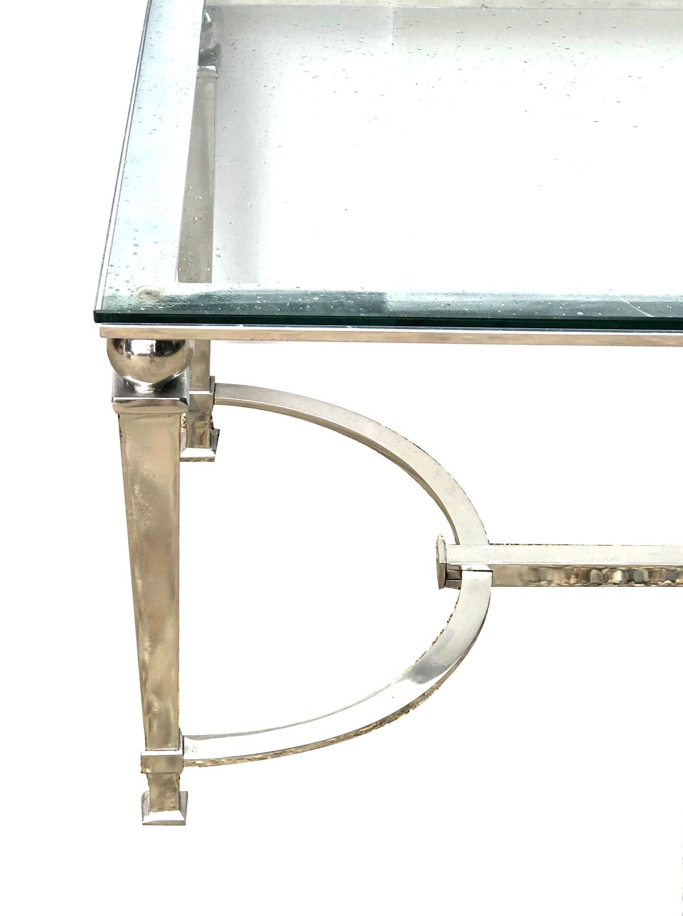 of art deco and neoclassical inspiration, the rectangular table with glass top resting on a sturdy chrome frame with tapering square-form legs capped with bold spheres; all joined by a shaped h-stretcher