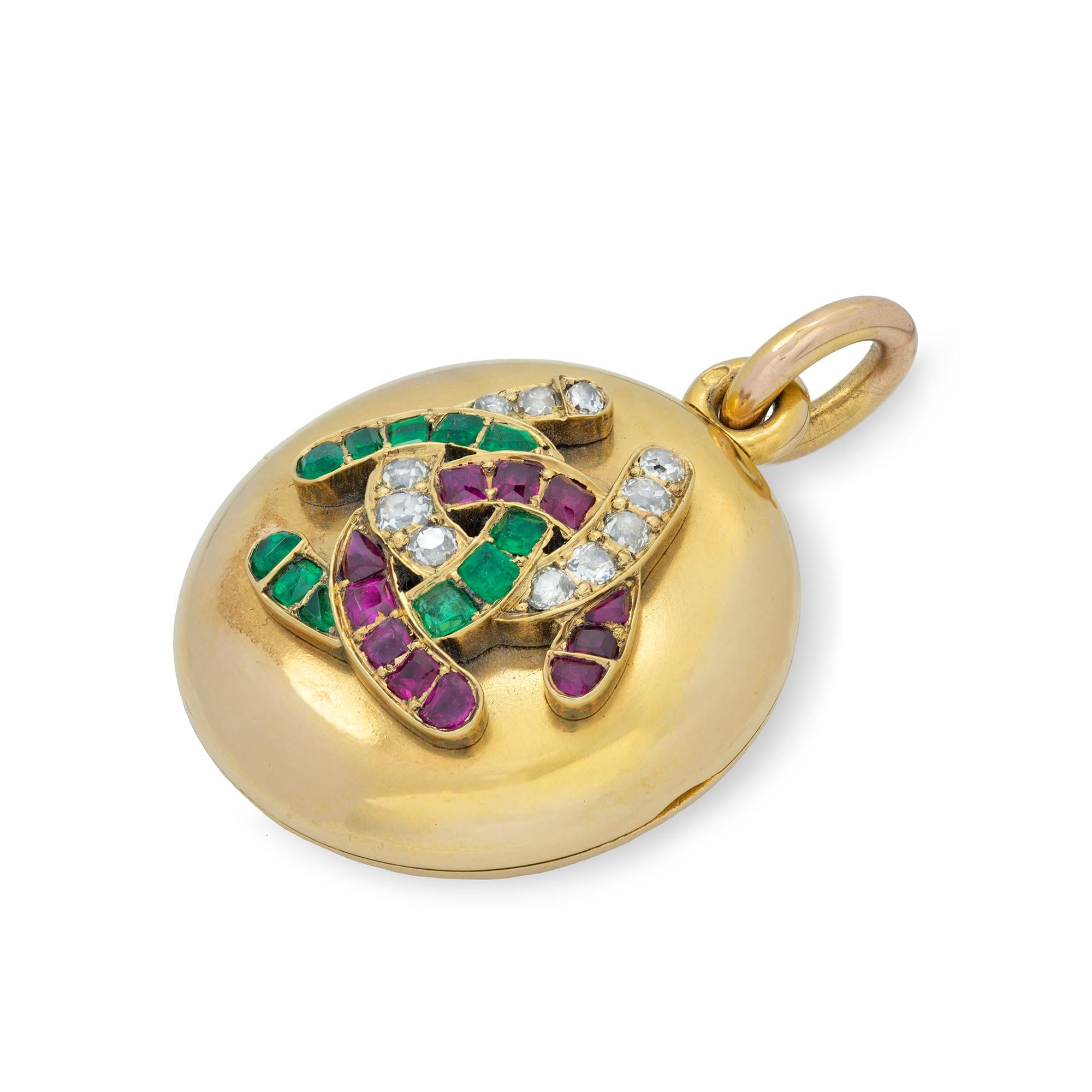 A French mid nineteenth century gold, ruby, emerald and diamond locket, the round satin-finish yellow gold locket set to the front with a motif of three interlocked horseshoes, one of emeralds, one of rubies, the other of diamonds, the locket