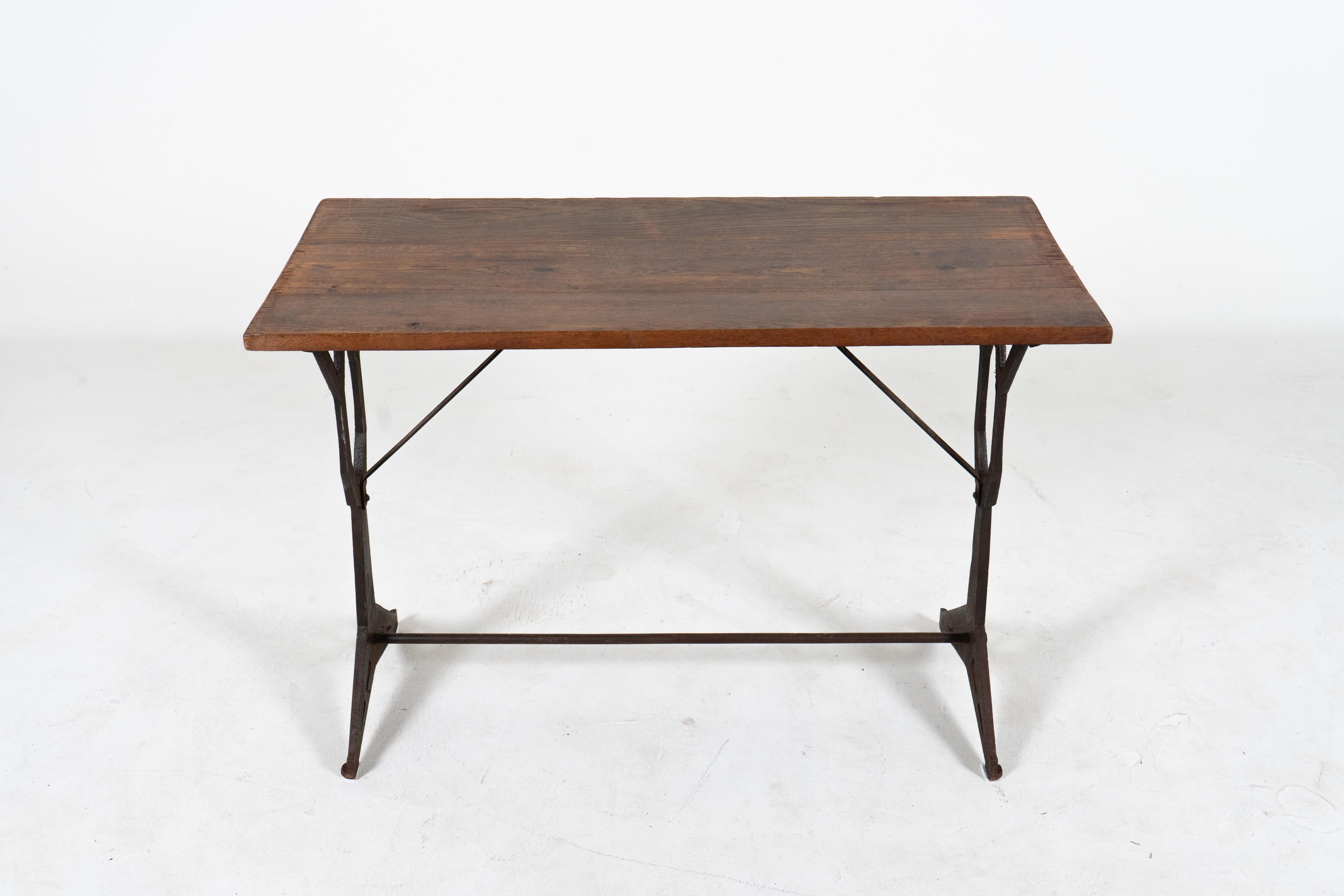 A charming vintage French bistro table from Paris with a thick rectangular slated oak wood top. This table has detailed cast iron legs with an x-shaped brace between the legs for support. The design of the legs is cubist -quite angular and unusual.