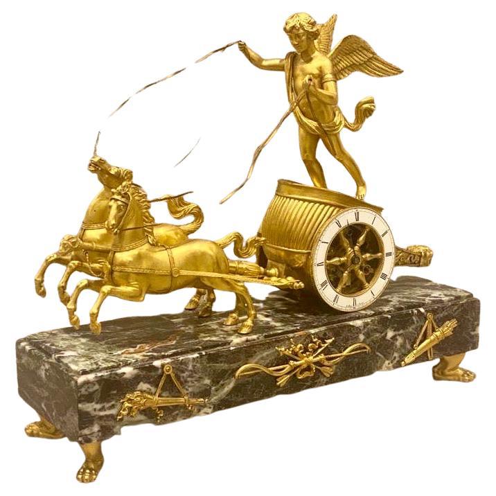 Pendule de char à sonnerie en bronze doré et marbre verde antico, CIRCA, milieu du 19e siècle. 
L'horloge est entièrement d'origine et possède encore son importante dorure d'origine.
Le boîtier représente Cupidon dans un char tiré par deux étalons,