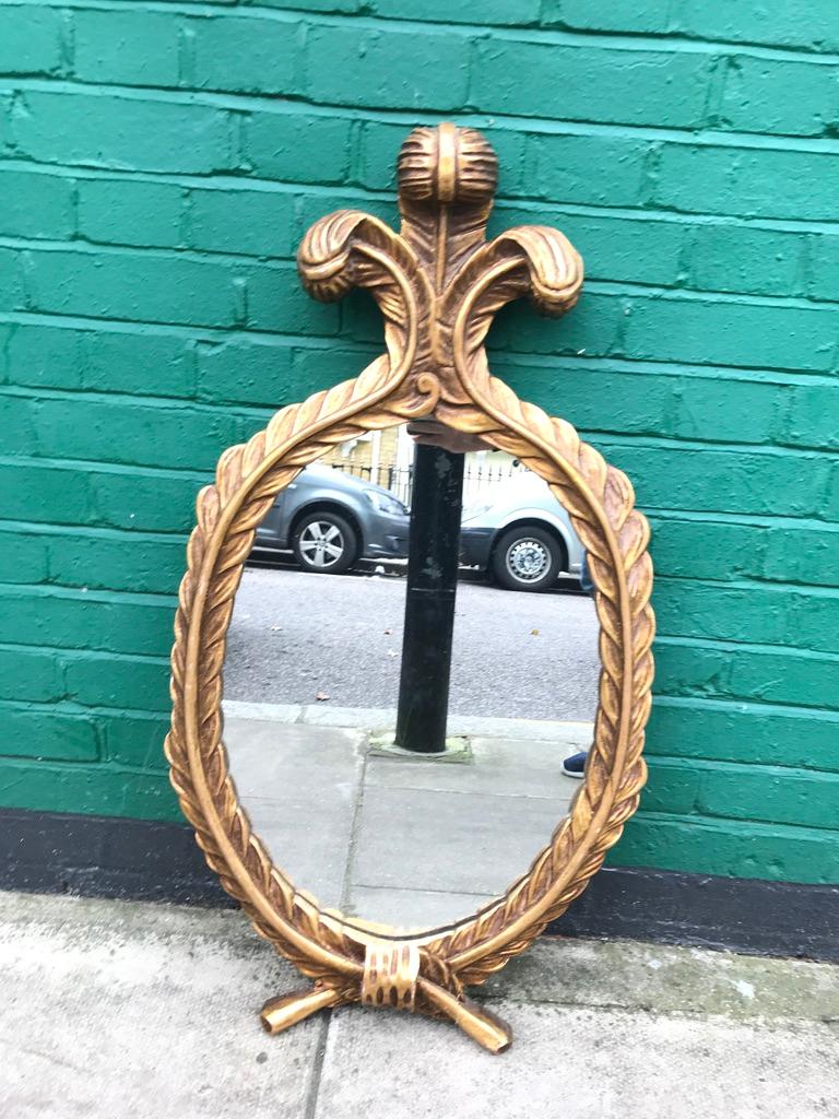 A French hand carved gold gilt oval wall mirror, with Fleur-de-lis feathers cascading down on to Laurel leaves, tied with a bow at the bottom.