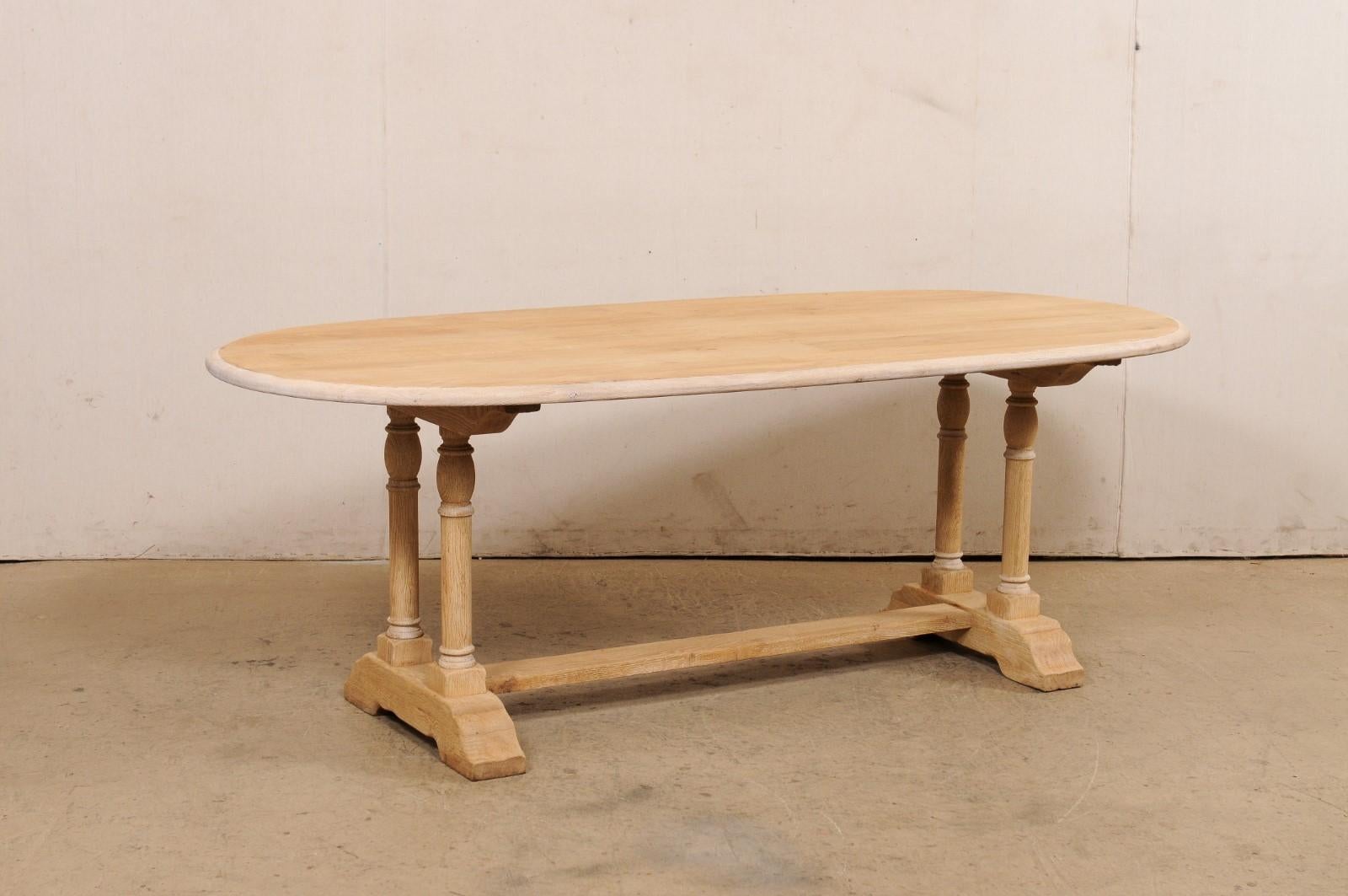 A French oval-shaped bleached oak dining table from the mid 20th century. This mid-century table from France features an oval-shaped top just over 6.75 foot long (approximately), which is presented upon trestle legs comprised of a pair of rounded