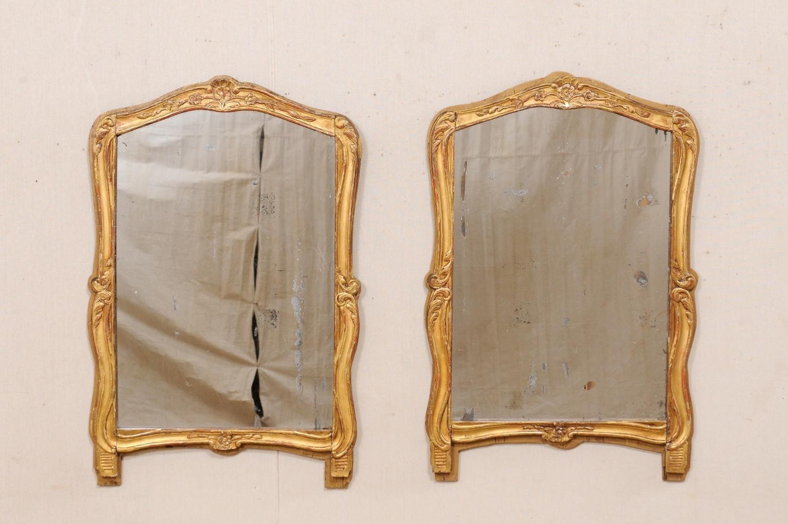 A French pair of carved wood mirrors with their original gilt finish from the 19th century. This antique pair of mirrors from France are both simple and elegant, having mostly rectangular shape, with a gentle movement along the sides and a