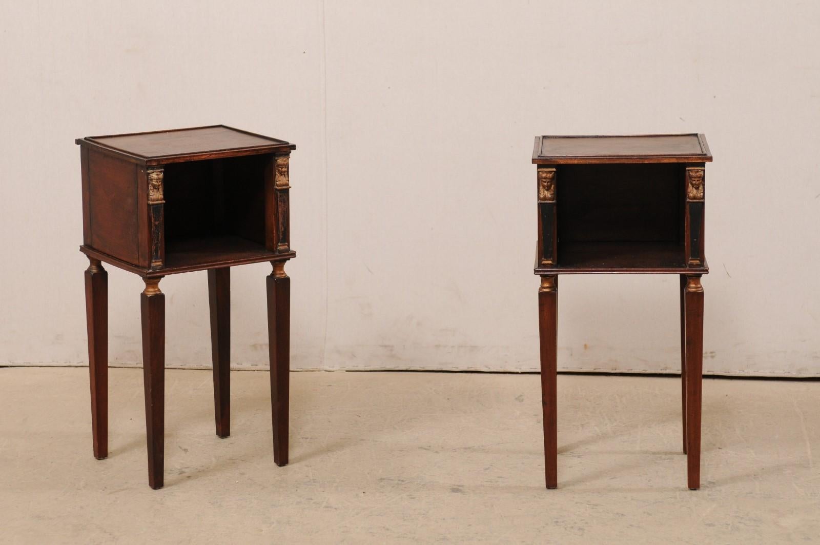 A French pair of smaller-sized side tables, with cubie shelf and Egyptian Revival accents, from the turn of the 19th and 20th century. This antique pair of tables from France each feature a mostly-square shaped top with subtle raised rim, resting