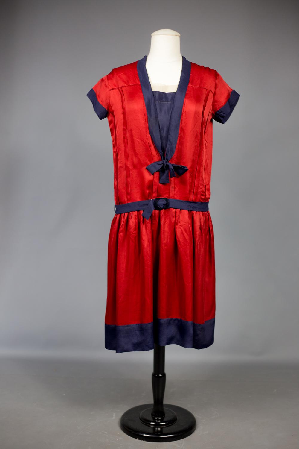 Circa 1920/1925
France
 
Beautiful sailor dress in cherry red Duchesse satin in the patriotic spirit of France after the First World War. Straight dress with short sleeve and pleated on the bust and underlined with navy crepe.. Sailor collar trimmed