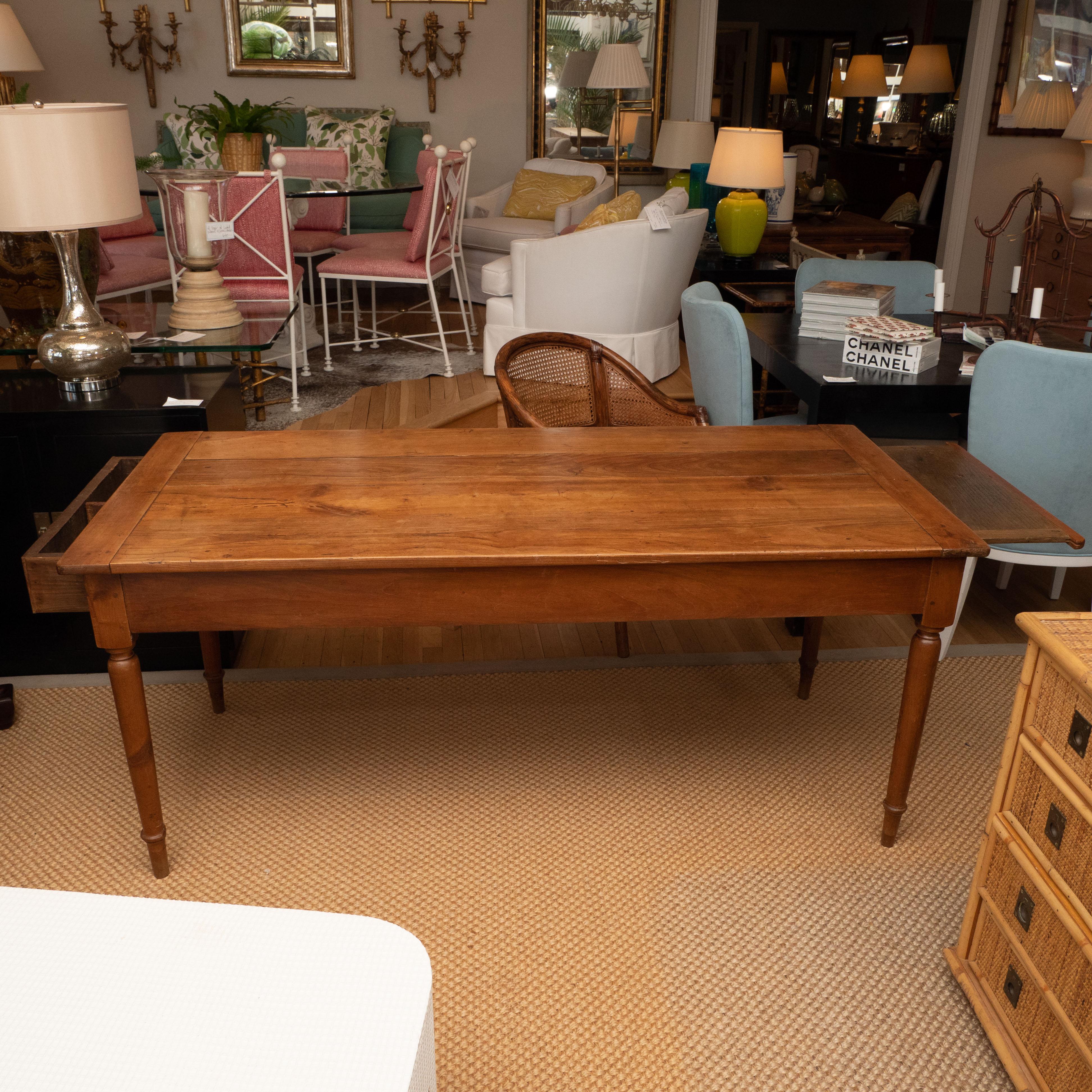 A nice looking farm table in cherry with tapered legs, featuring a drawer on one end and a pull-out tray on the other end. The table has worn to a lovely warm patina and Its clean lines make it suitable for both traditional and contemporary settings.