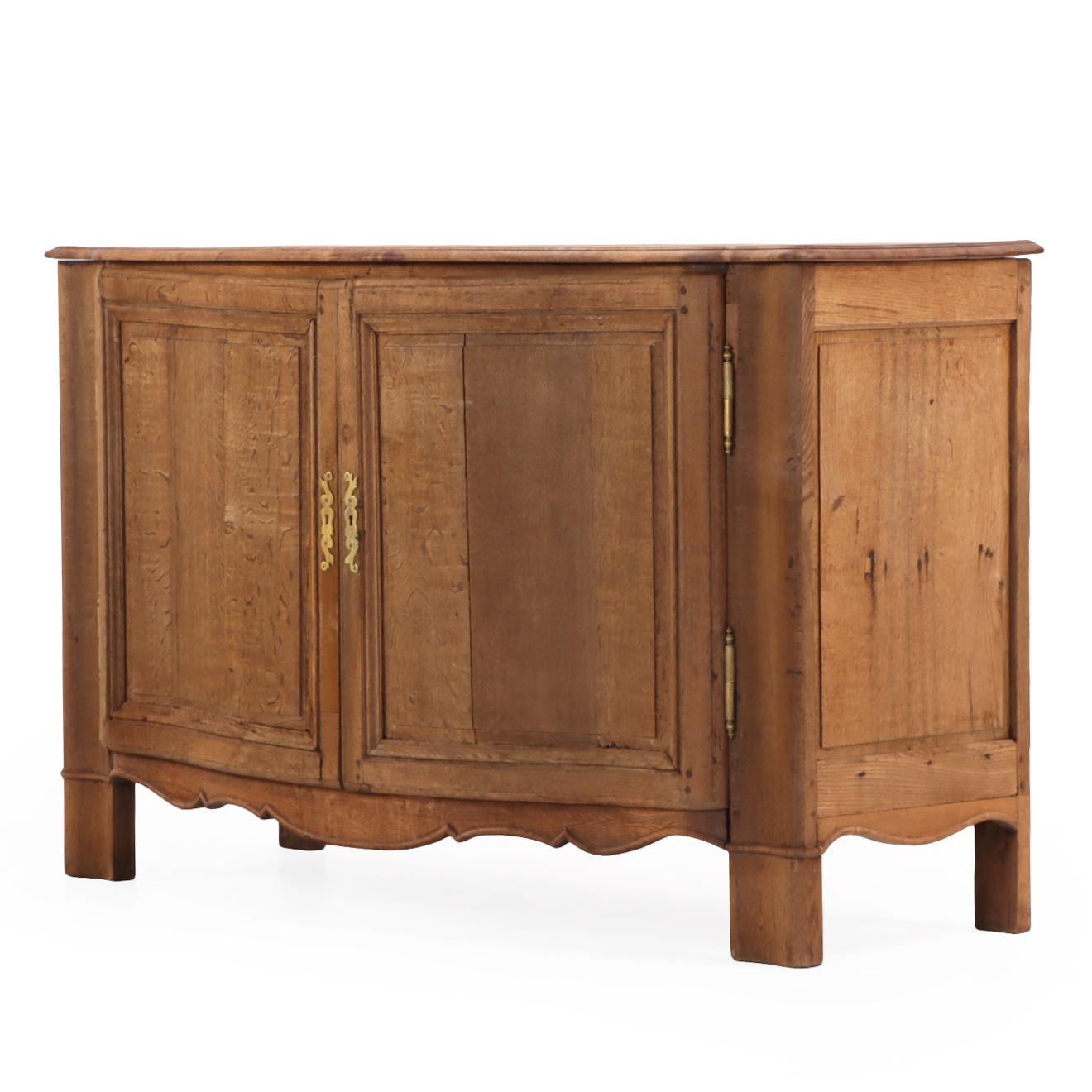 Featuring a shaped top above carved paneled doors and an elegantly scalloped apron, this piece rests on short stile form legs. The oak has been stripped to a natural finish, revealing its warm grain and rustic character, typical of the French