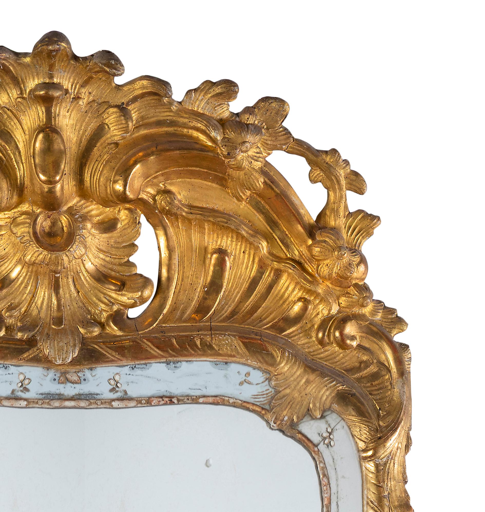 A French Régence Gilt Hall Mirror, 18th Century

Description:
The narrow rectangular plate with rounded corners at its summit, within a gilt reed-and-reel moulding extending to a mirrored surround applied with gilt floral mounts and painted linear