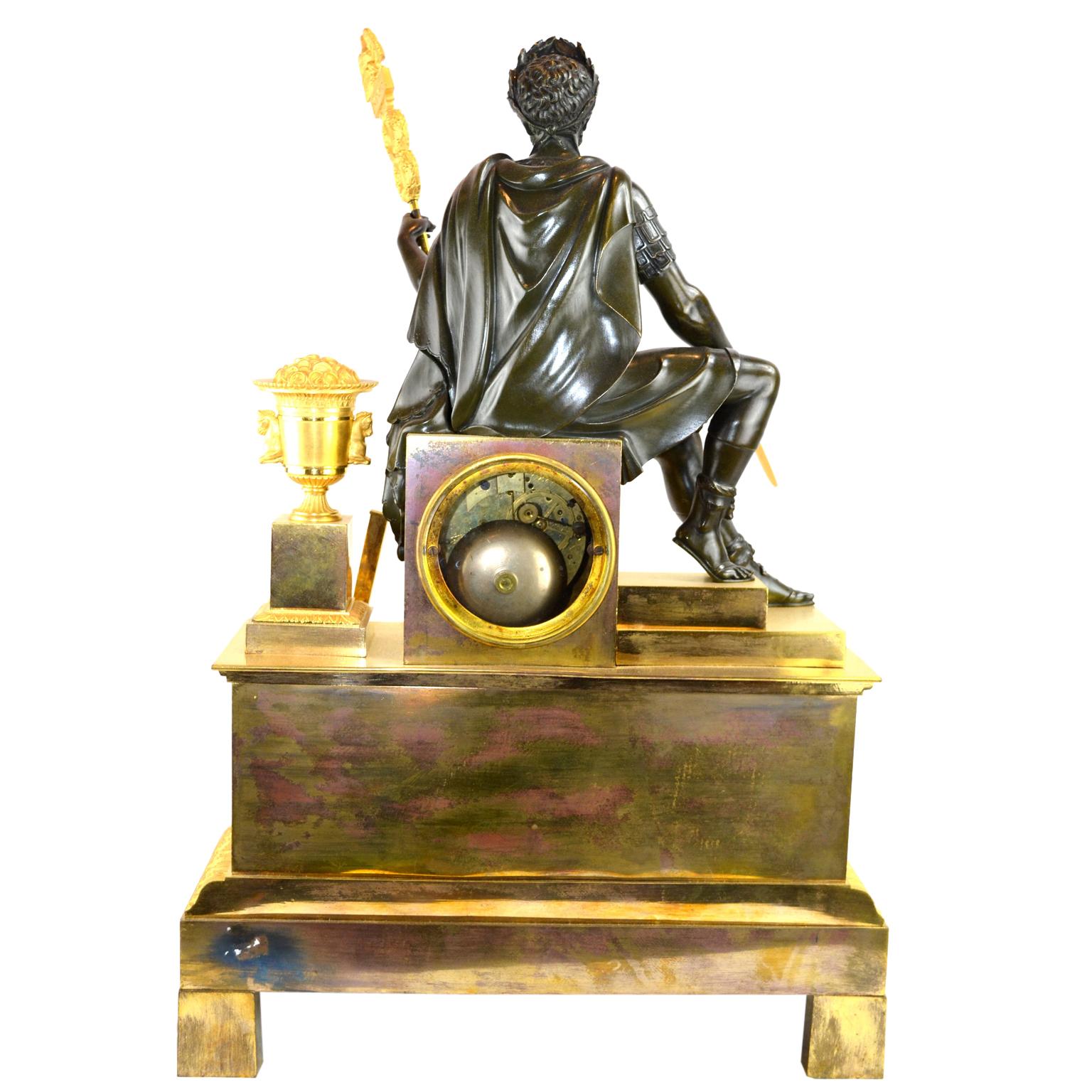 Pendule de cheminée de la fin de la période de l'Empire français représentant un empereur romain assis, en bronze patiné finement ciselé, tenant une épée dans une main et une bannière romaine dans l'autre. Il repose sur un socle rectangulaire qui