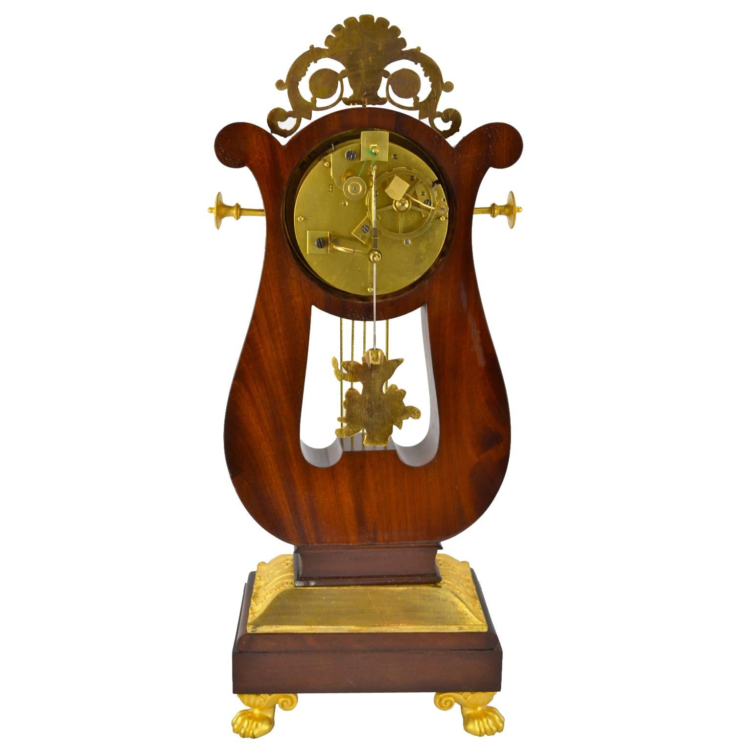 A high quality Restauration period mahogany and gilt bronze lyre mantel (fireplace) clock in the shape of a lyre. The mahogany case is highly decorated in gilded bronze; the lyre sits on a rectangular base over a large gilt bronze border, the base