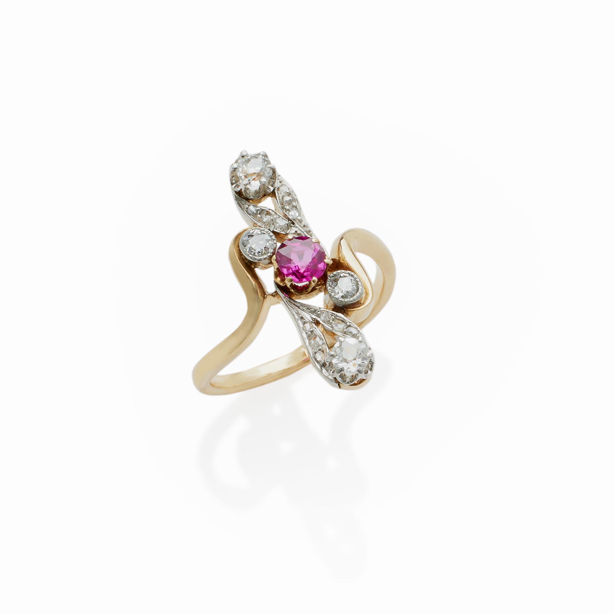 This French ruby and diamond ring in platinum-topped 18K gold dates from circa 1910. The slender form centers a ruby surrounded by swirling gold vines and a pair of stylized old European and rose-cut diamond blossoms. The graceful form, imbued with