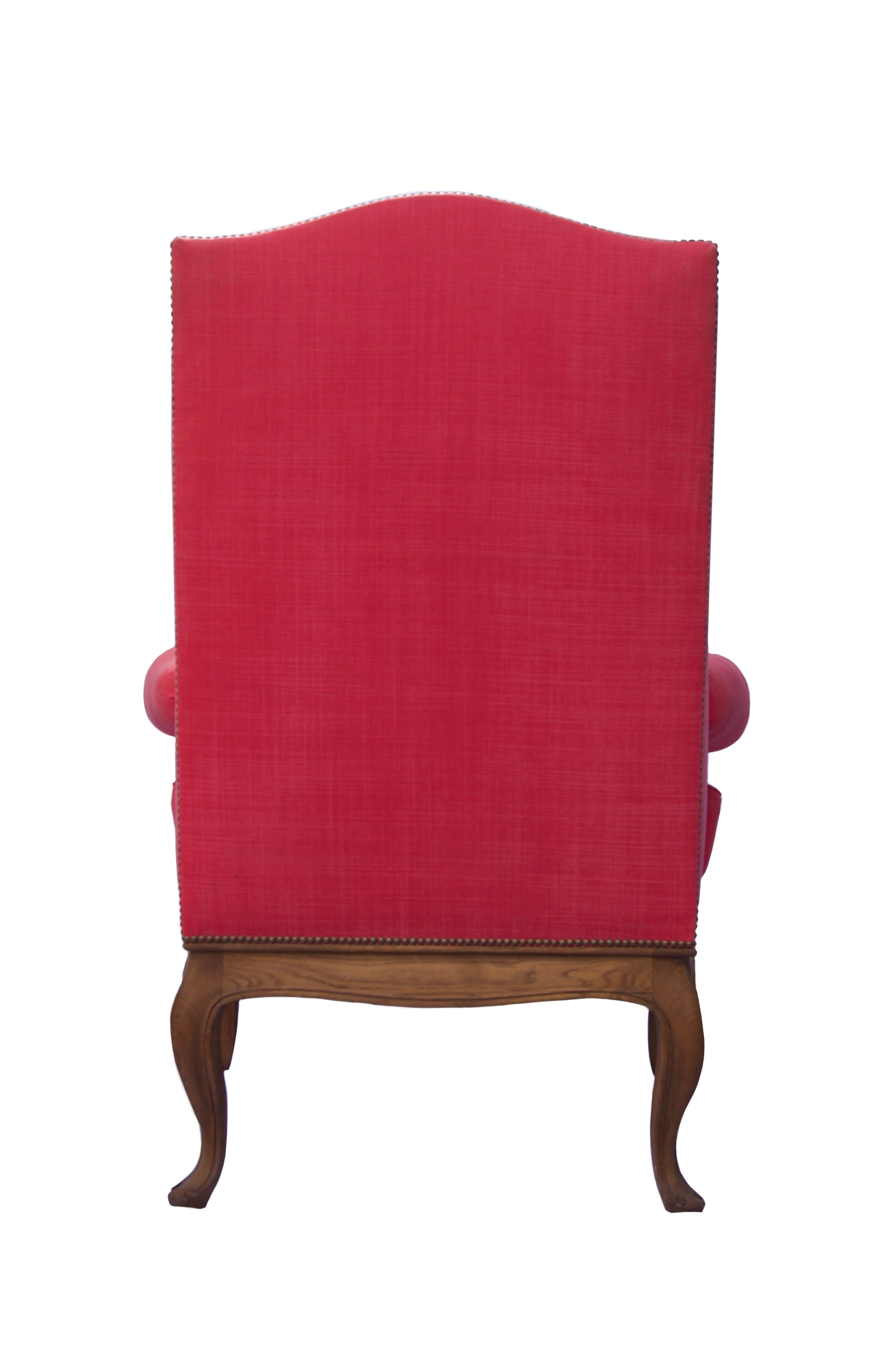A French style oak wing chair covered in pink linen fabric with natural oak legs.