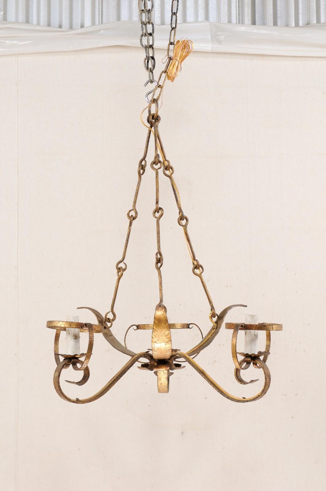 A French three-light chandelier from the mid-20th century. This vintage hanging light from France features three scrolled light arms which are divided by a beautiful splay of three iron leaves between them, creating a small circular center, giving