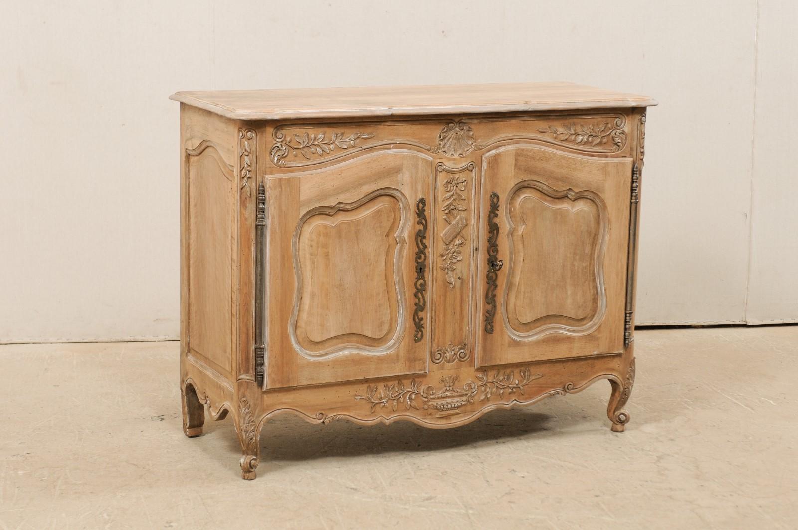 A French two-door bleached wood buffet cabinet from the mid-20th century. This vintage cabinet from France features a subtly scalloped edge top, which rests above a case which houses a pair of arched paneled doors, surrounded within abundantly