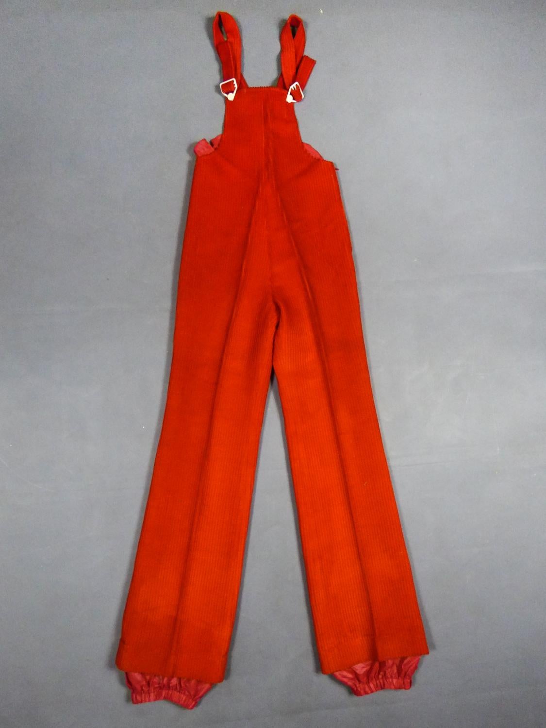 Circa 1975
France

Jumpsuit in vermilion red ribbed velvet from the Jantzen brand, dating from the 1970s. The Top tightened with white plastic buttons and straps with loops. Skin-tight cut with flared pants whose folds remain well marked. Closure on