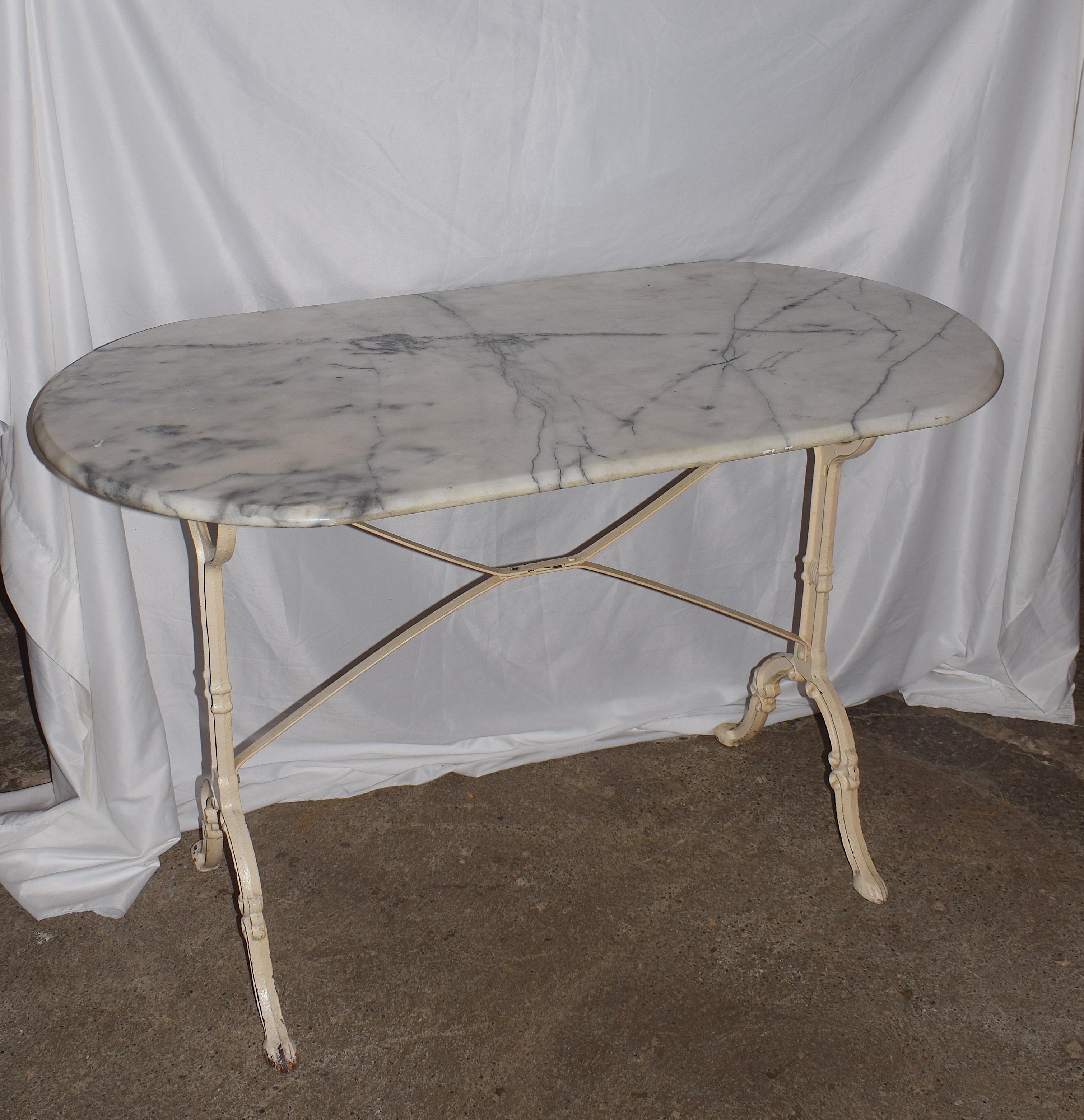 This French bistro table has an oval marble top it dates from the early 20th century. Its marble top rests on a heavy iron based that is painted in a soft cream colour which has gone mustard. In places due to rust, this patina effect adds another