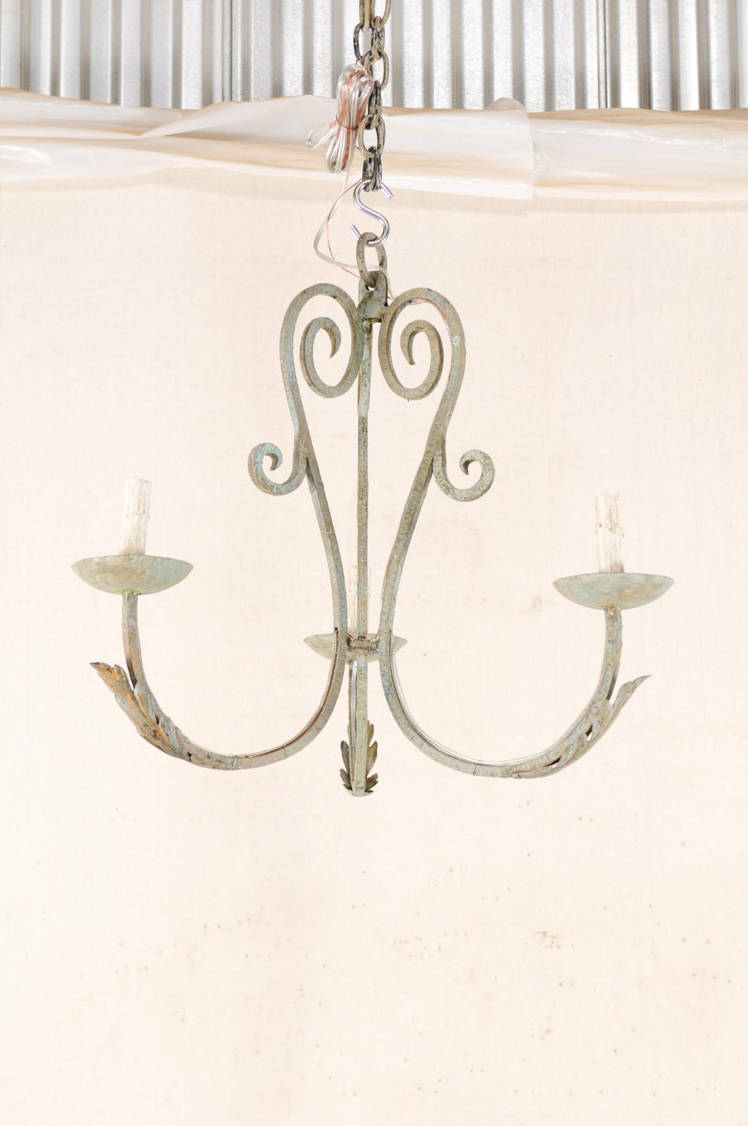 A French three-light painted iron chandelier from the mid-20th century. This vintage hanging light from France is made of three swagging arms that join together at the center creating a visually open column, adorn with various scrolls. Each of the