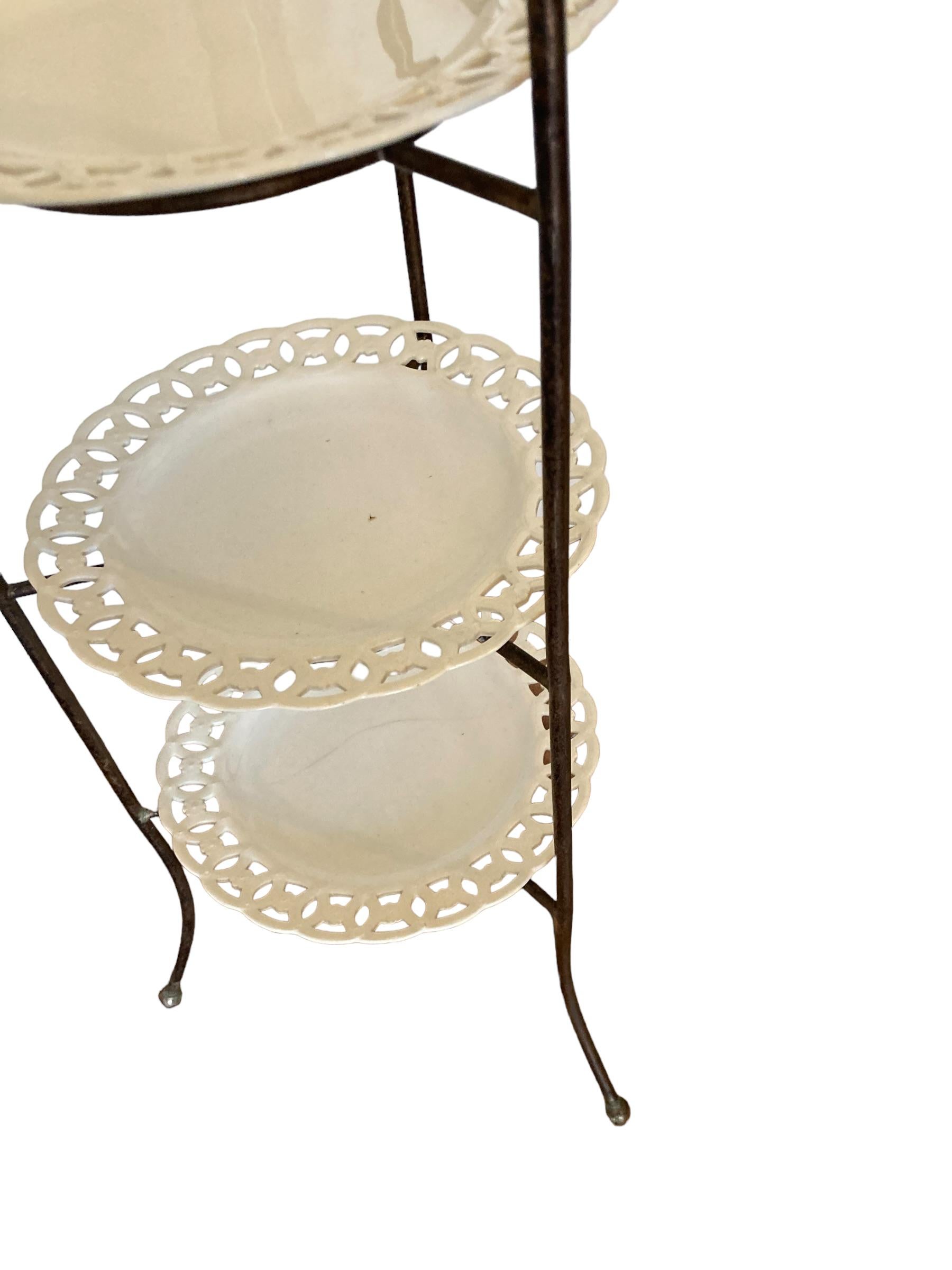 French Wrought Iron three tier cake stand with ornate porcelain plates. This elegant three-tiered cake stand, a perfect addition to any special occasion or afternoon tea. Beautifully designed, this stand features three plates, allowing you to