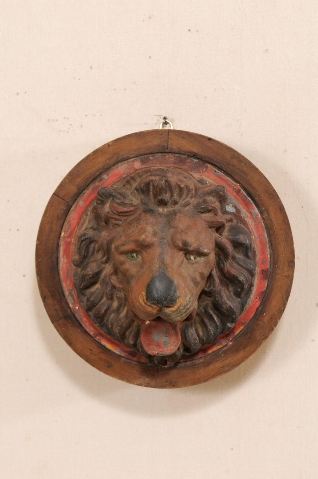 A French lion head wall-mounted zinc and wood plaque from the early 20th century. This antique wall ornament from France features a painted zinc lion head, with full bushy mane, expressive eyes, and opened mouthed with tongue hanging out. The zinc