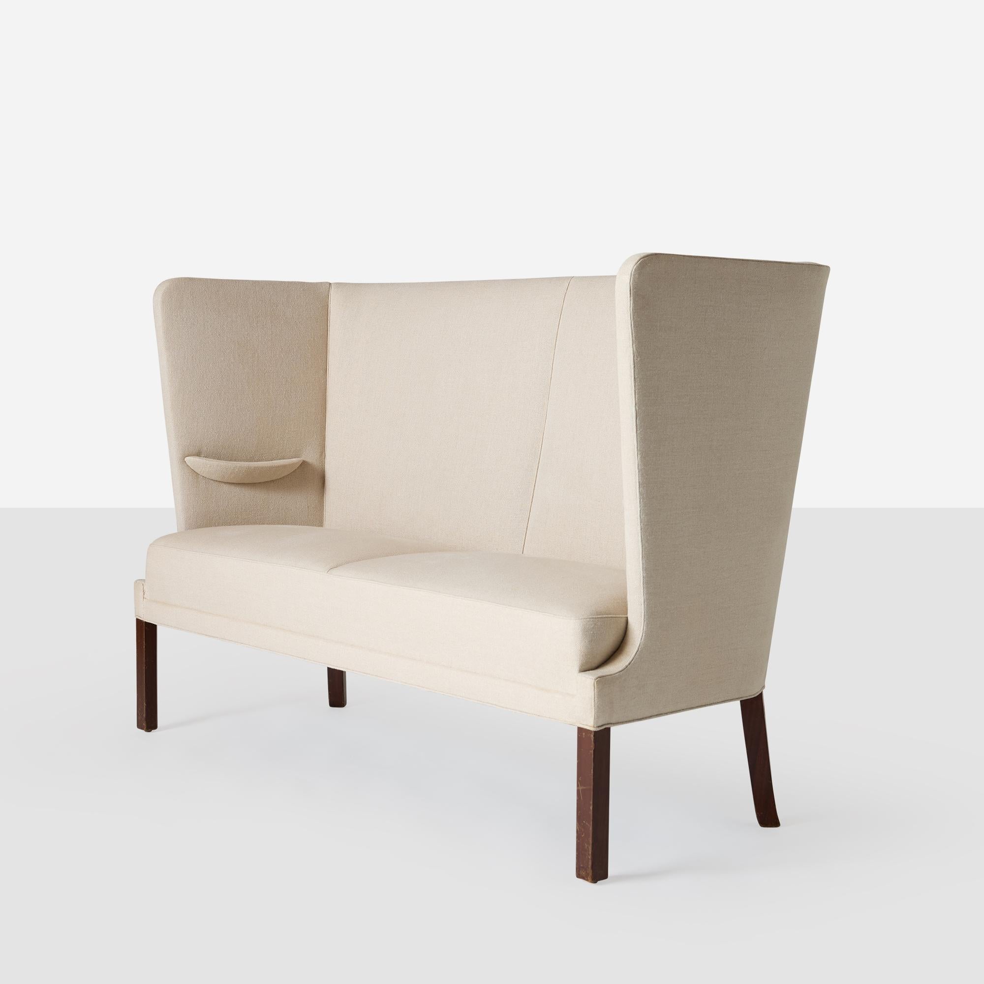 Canapé à haut dossier conçu par Fabrice Henningsen, avec un revêtement en tissu de lin et des pieds en acajou noirci. Produite par le célèbre maître ébéniste danois, cette pièce témoigne d'un savoir-faire exceptionnel et d'un design minimaliste.