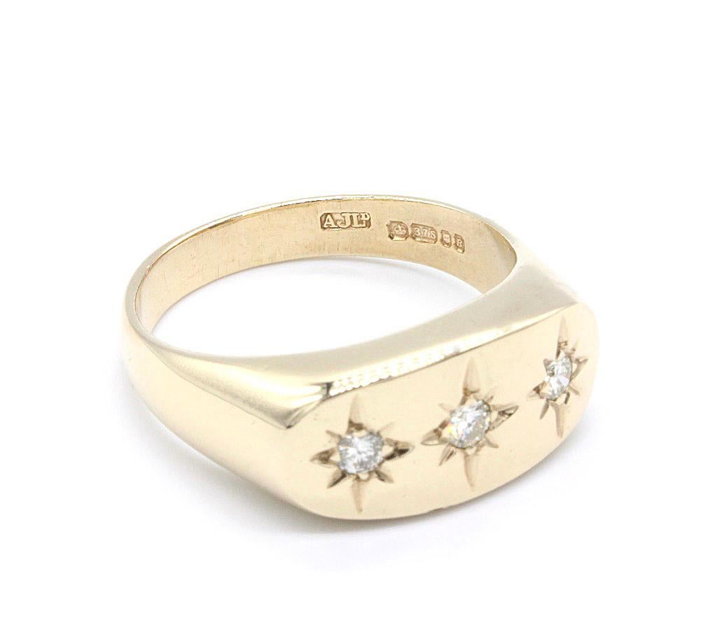 A Gentlemans 9Kt Yellow Gold Star Set Three Diamond Ring. The three round cut diamonds set in a row and enhanced by gold star settings. 
Hallmarked London 1975-1998   Maker AJLd.
Weight 9.86g   Diamonds approx 0.3Ct
Size UK U
Size USA 10 1/4