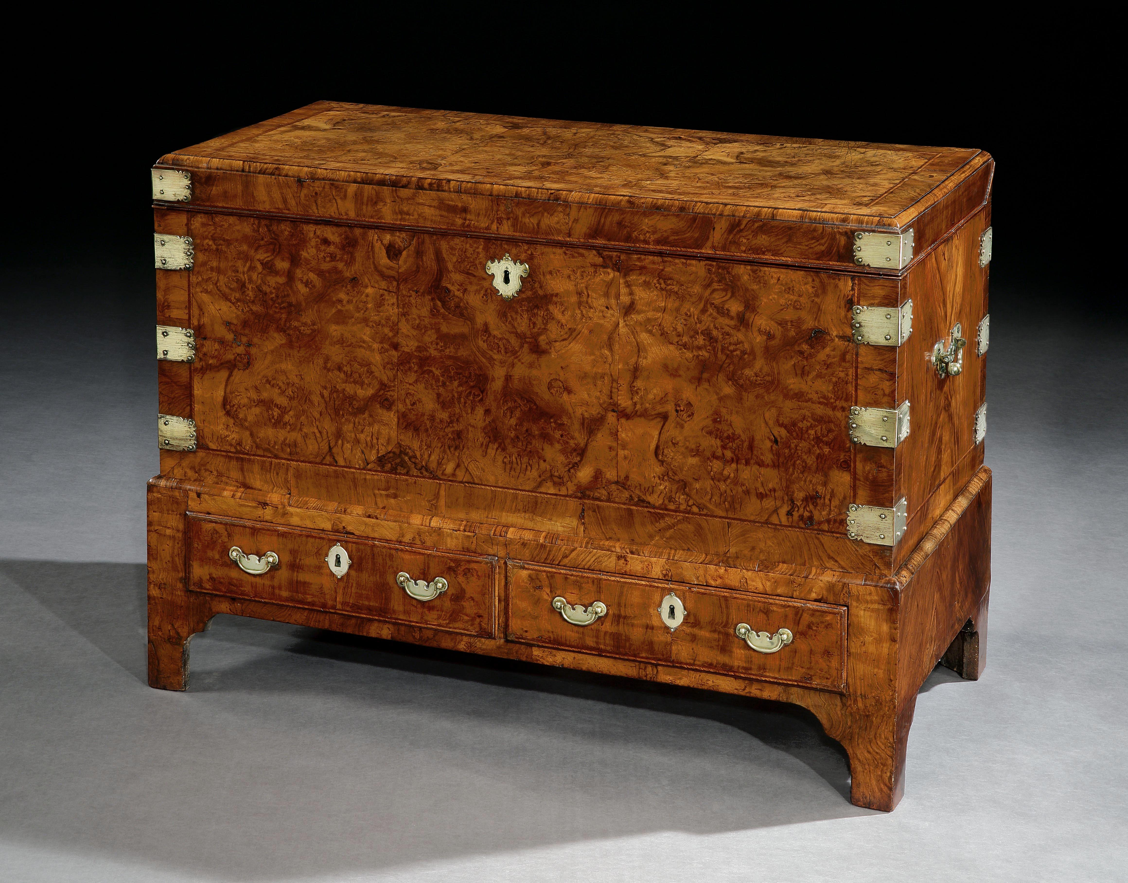 An early 18th century coffer on stand in richly figured walnut crossbanded throughout with feather bandings. The hinged upper part with brass-mounted corners and carrying handles. The lower part is fitted with two drawers with brass handles and